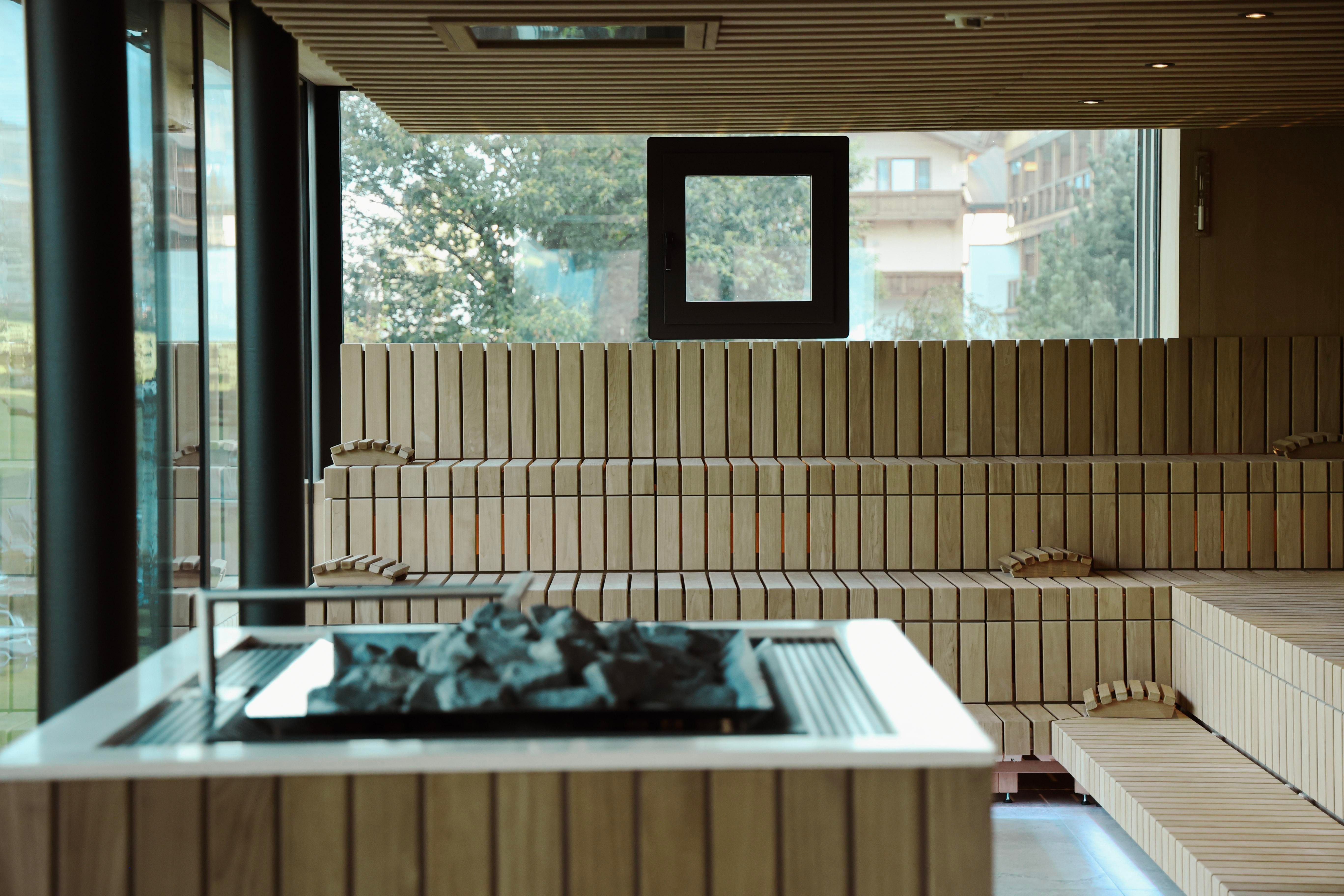 A modern spa with a wooden bench and a fire pit in the middle. Large windows provide plenty of light and a view outside.