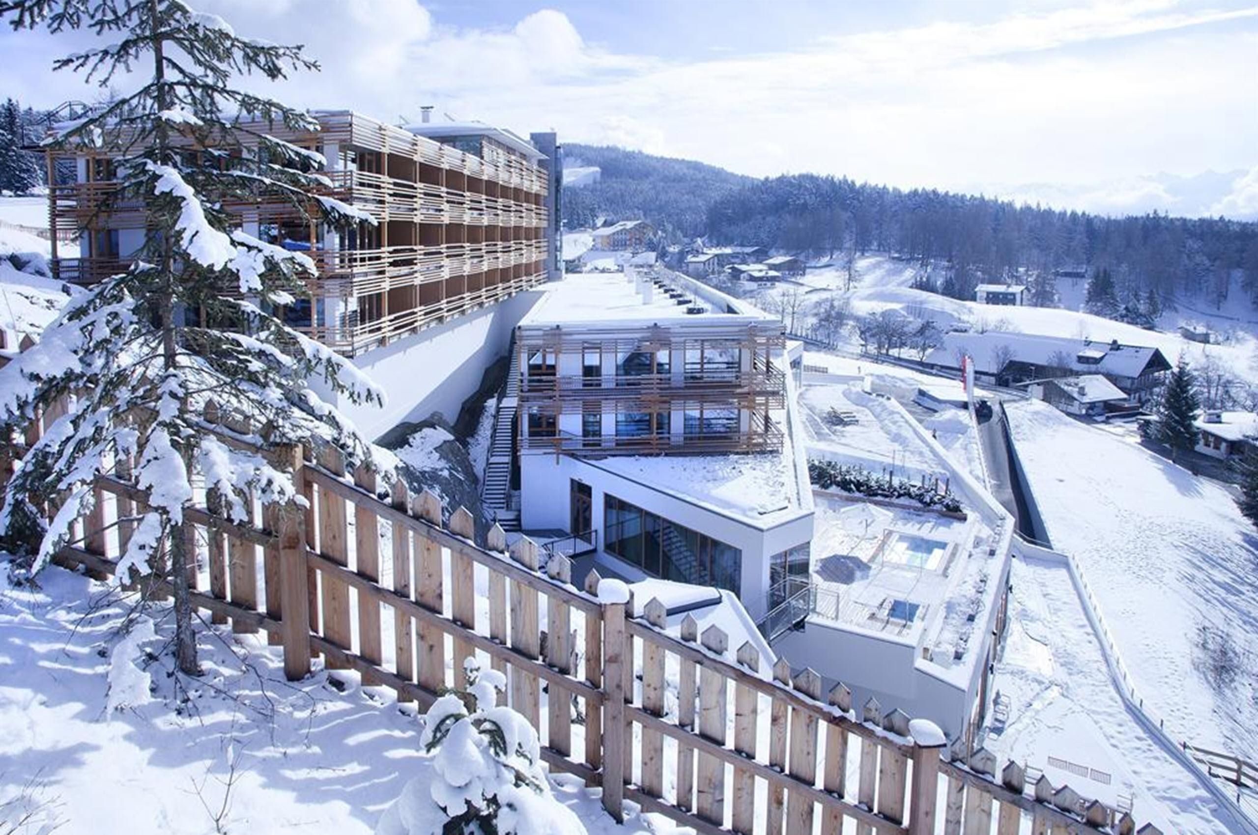 A modern hotel in a snow-covered landscape. In the background, gentle hills stretch out under a clear sky.