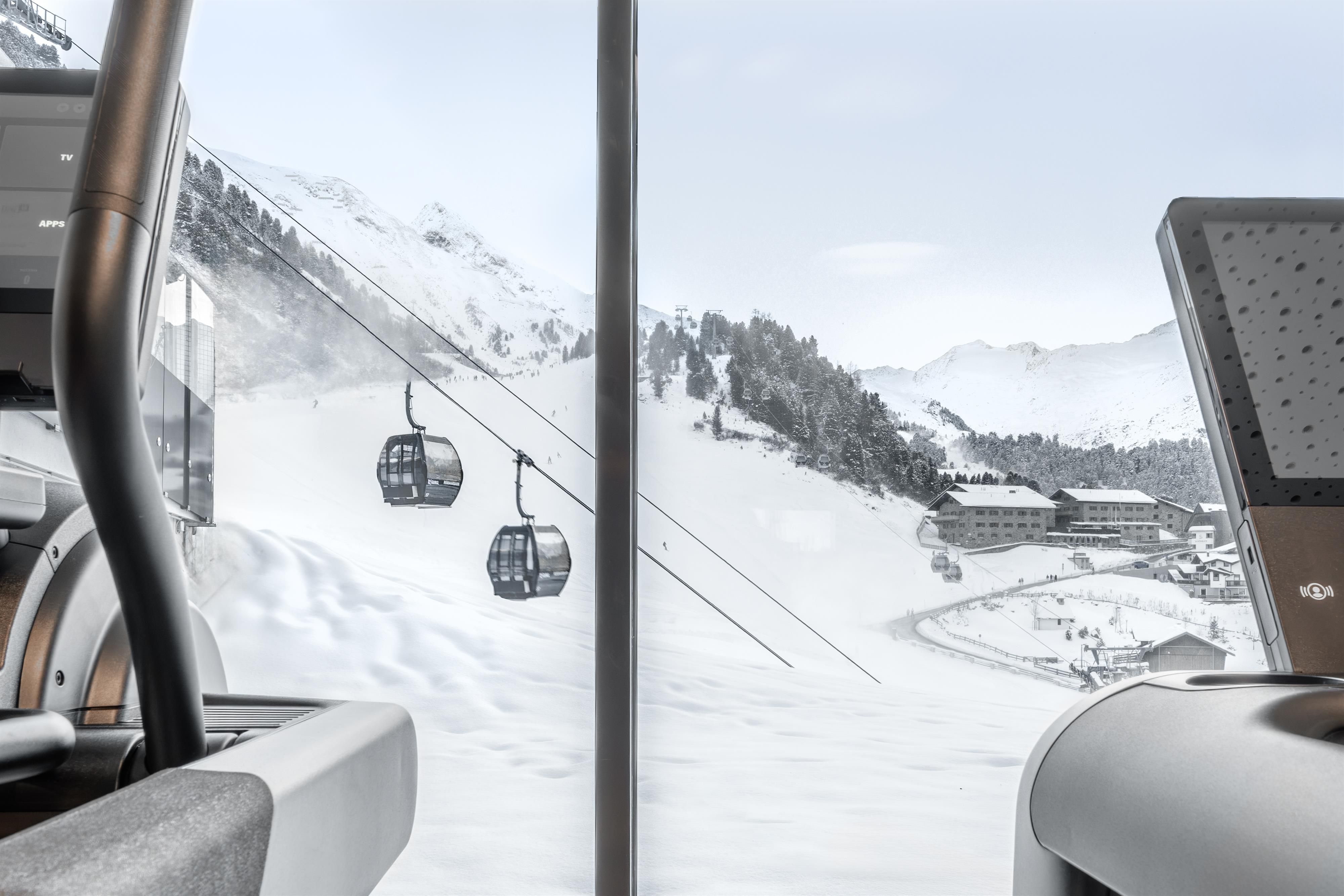 A view of snow-covered mountains with a cable car in the background. In the foreground, modern fitness equipment is visible.