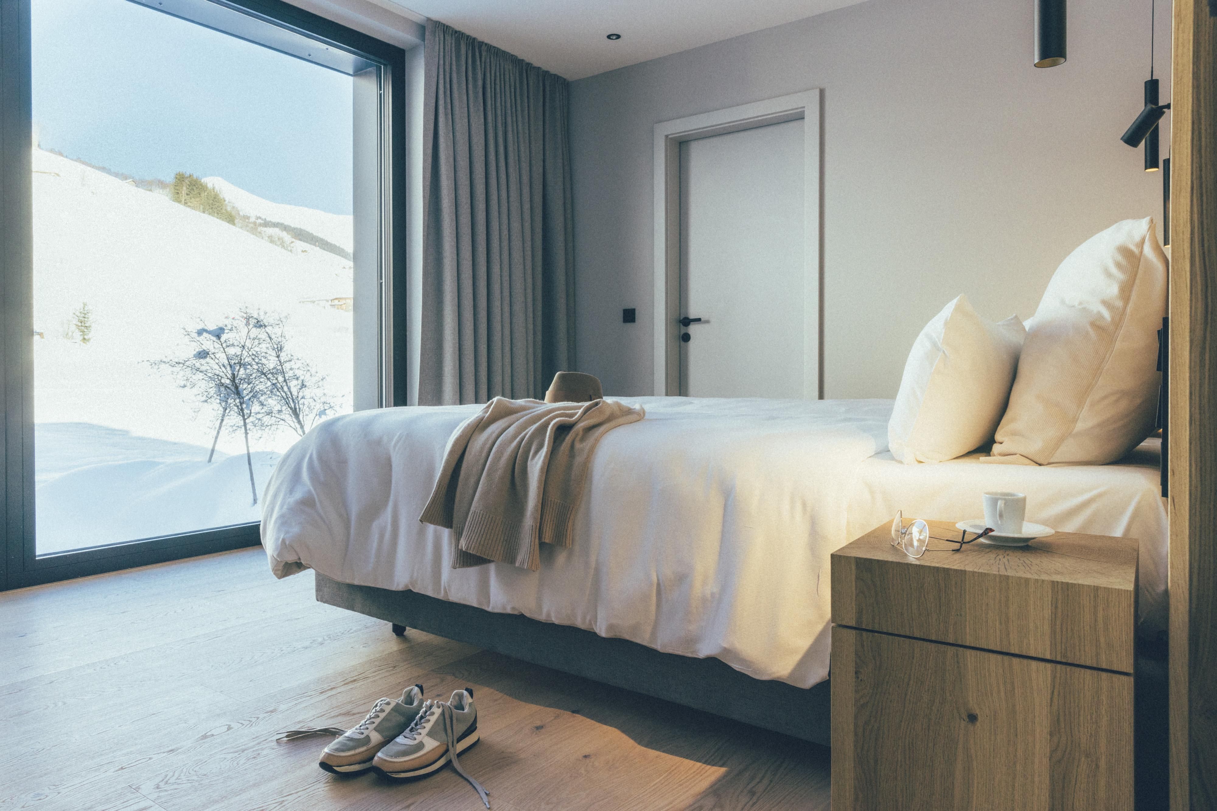 An inviting bedroom with a large window that offers a view of snow-covered landscapes. The bed is cozy and surrounded by neutral colors.