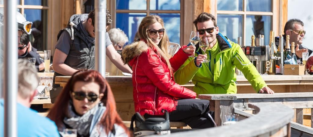 A sunny day in an outdoor bar with guests in winter clothing. A couple enjoys drinks and has fun together.
