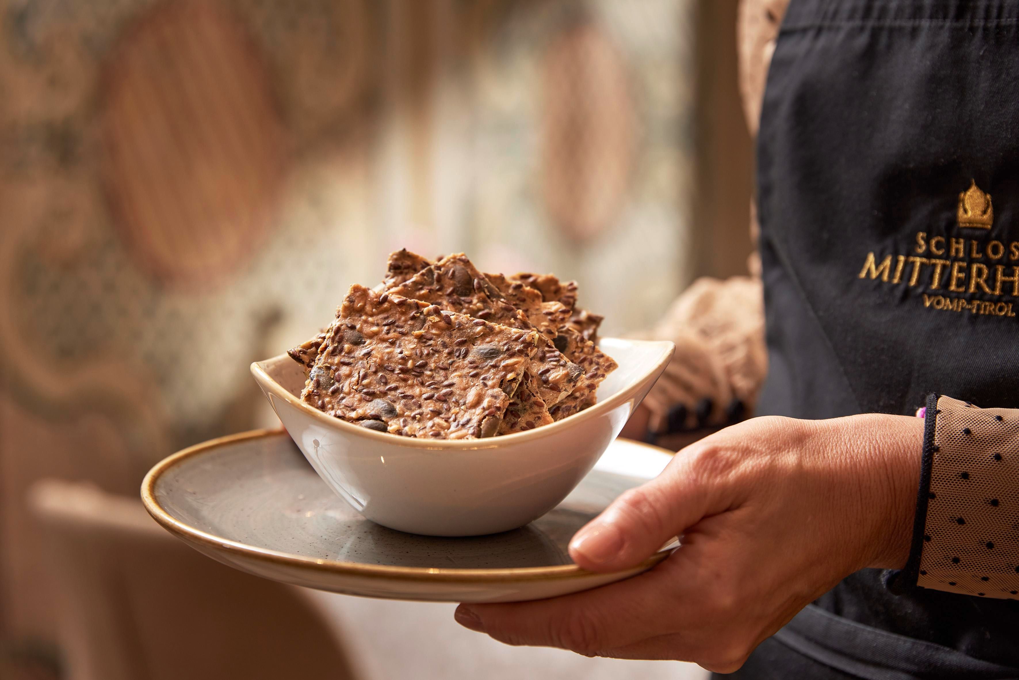 A person is holding a bowl with a portion of chocolate or sweets. The bowl is on an elegant plate and the background is tastefully decorated.