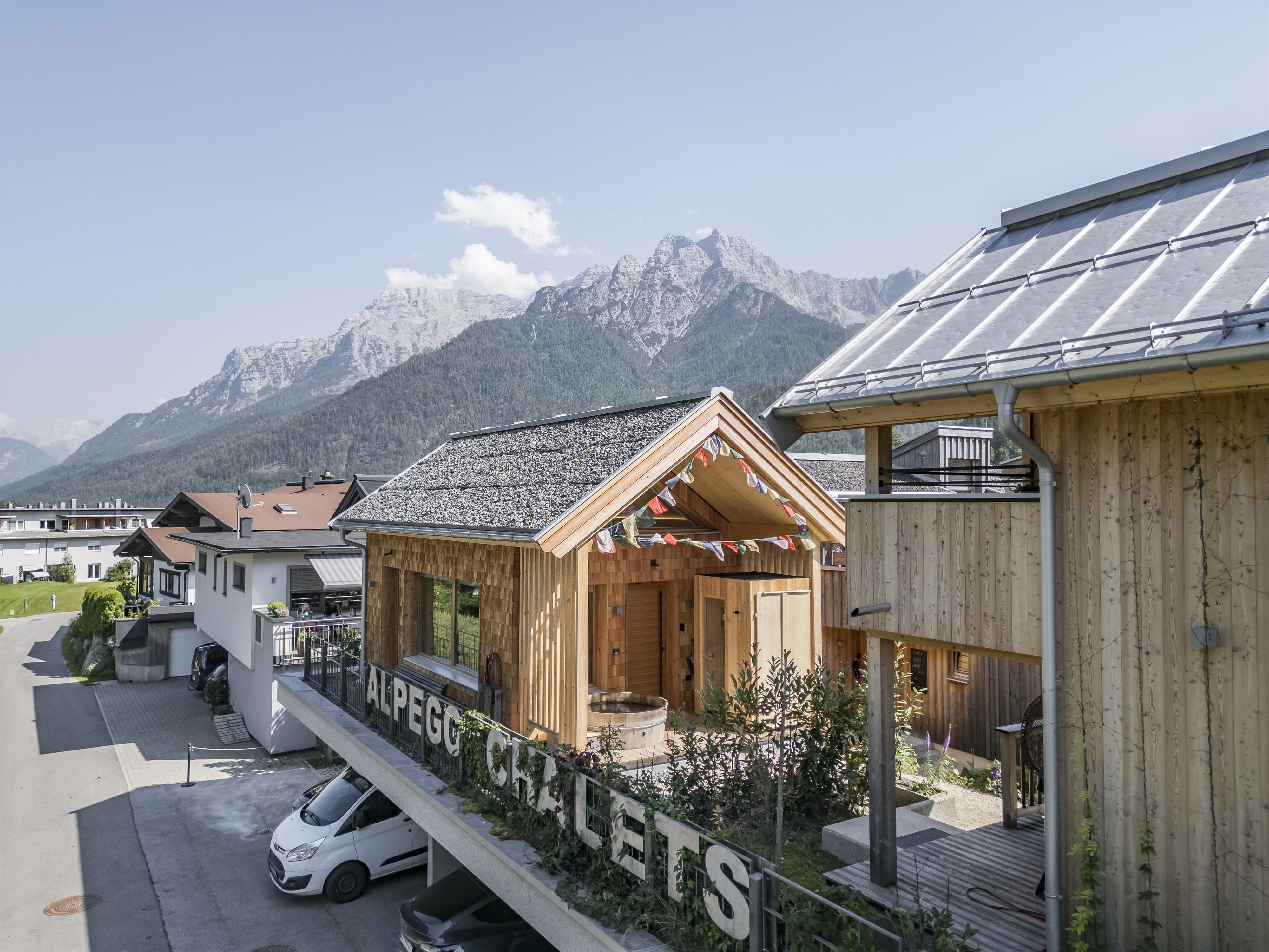 A modern wooden chalet set against an impressive mountain backdrop. The sun is shining and the sky is clear.