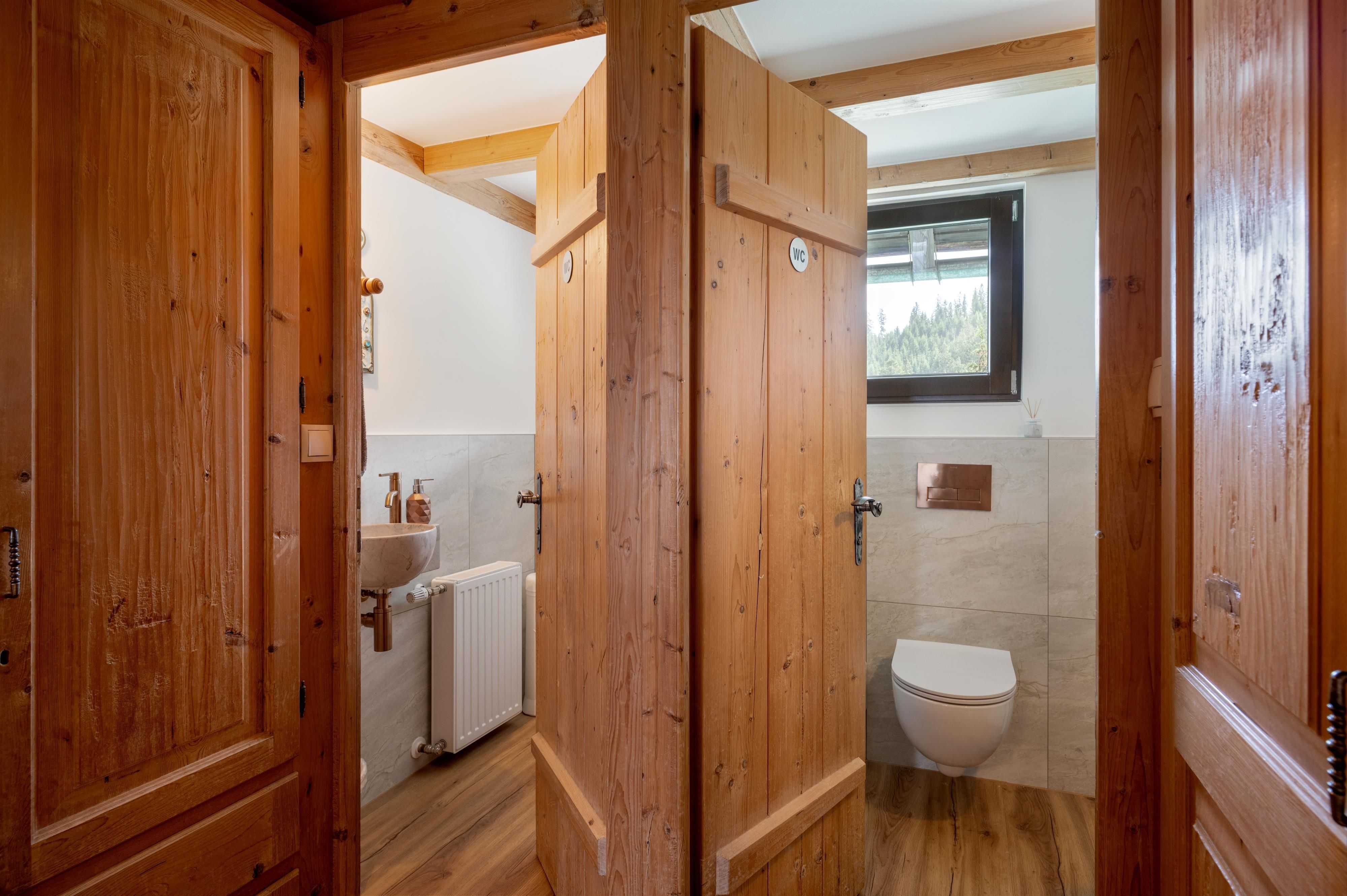 A modern bathroom with wooden paneling. There is a toilet and a shower that are separated by wooden walls.