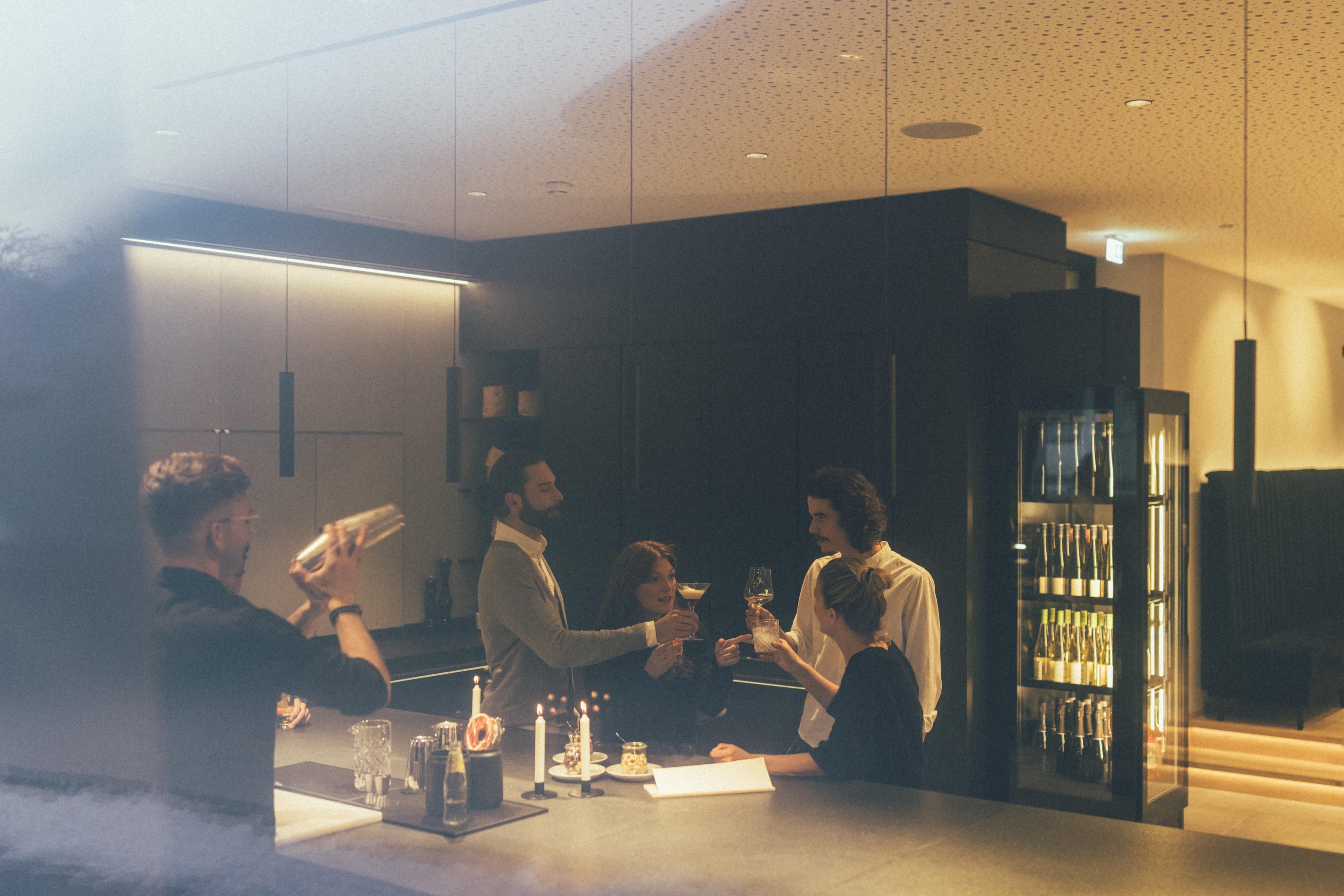 A group of people is standing at a bar and enjoying drinks. The atmosphere is modern and inviting.