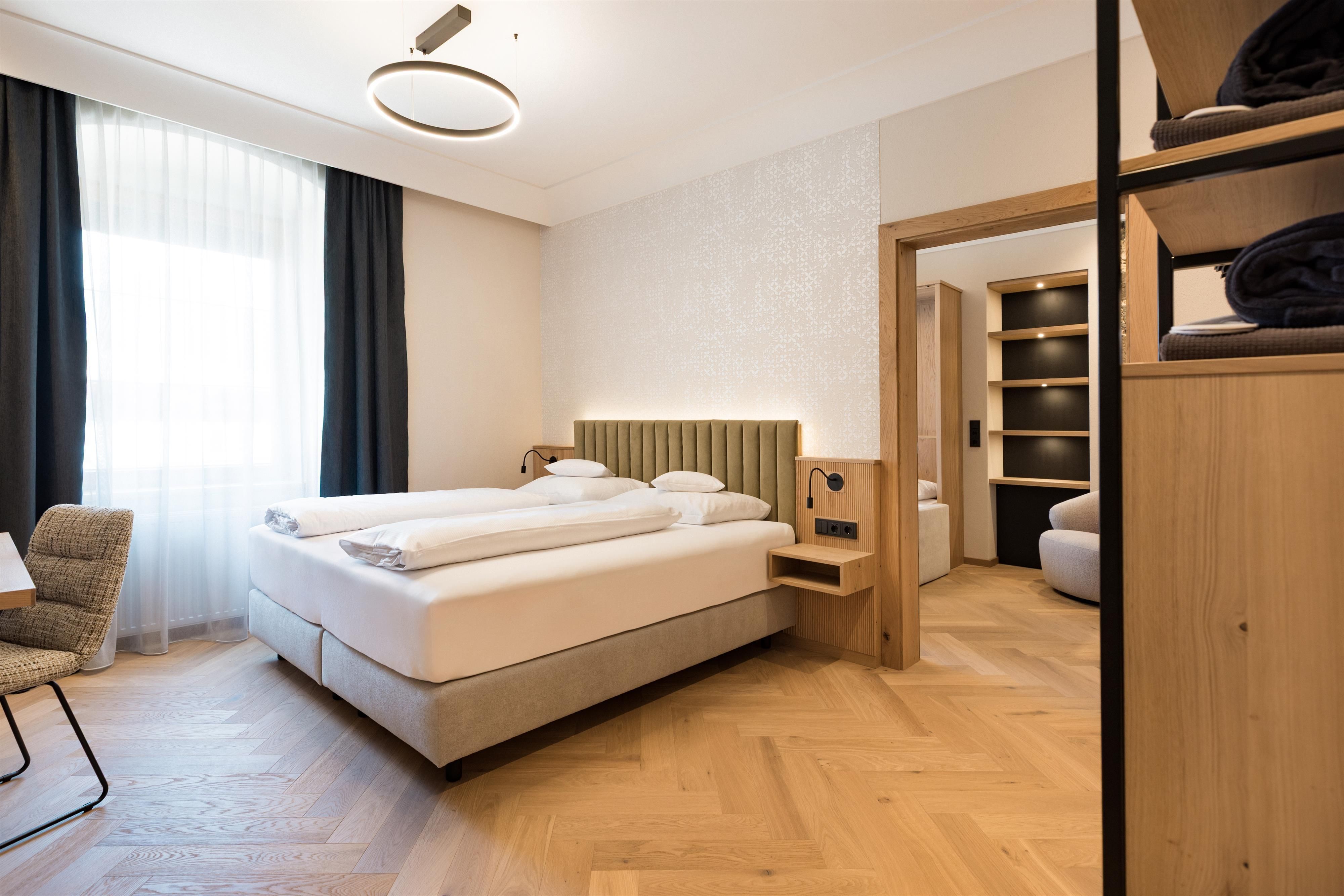 A modern bedroom with a comfortable double bed and wooden floor. Large windows provide plenty of daylight and a pleasant atmosphere.