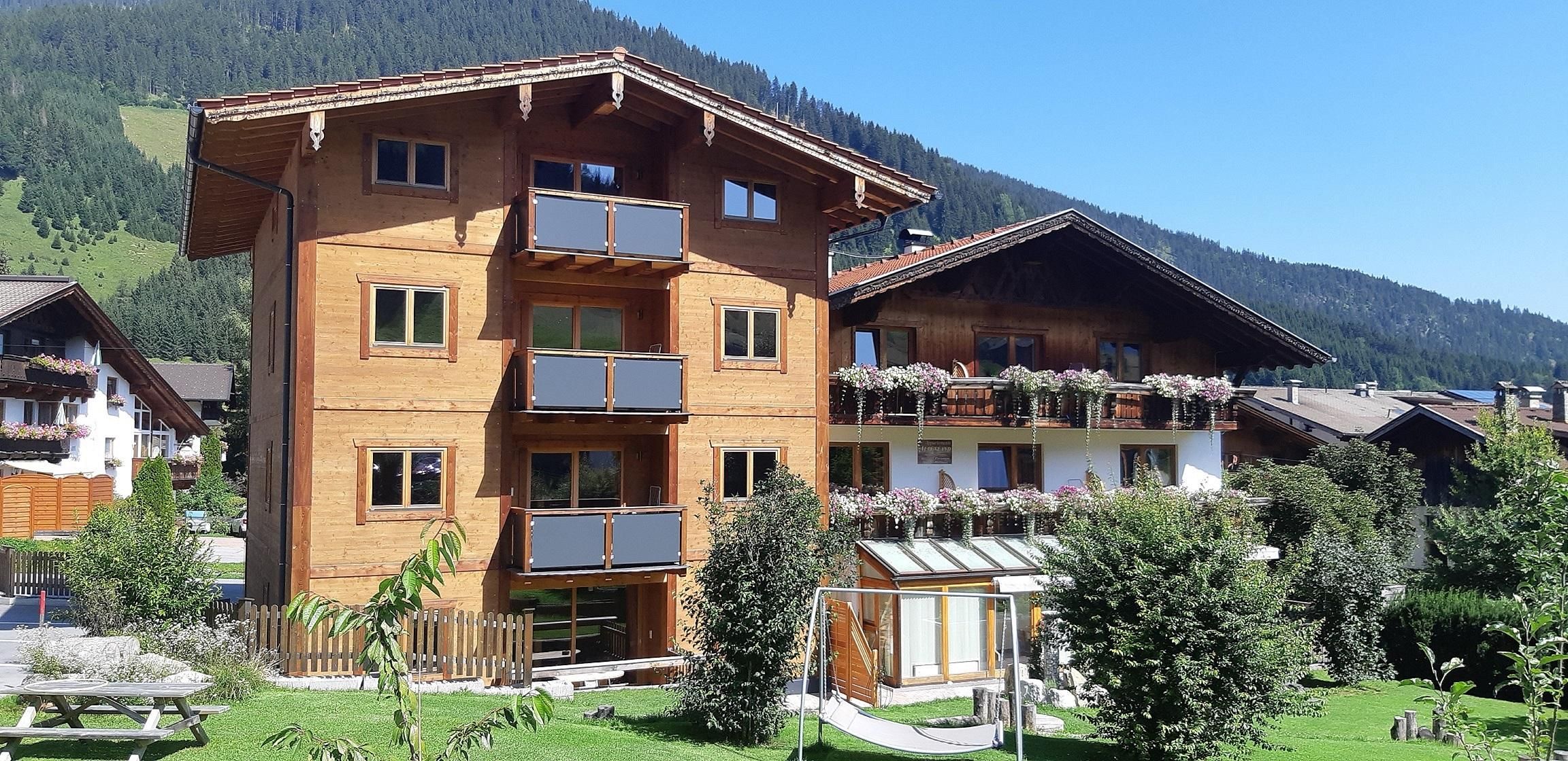 A traditional wooden house with several balconies and beautiful floral decorations. Surrounded by green landscapes and trees, it conveys an inviting atmosphere.