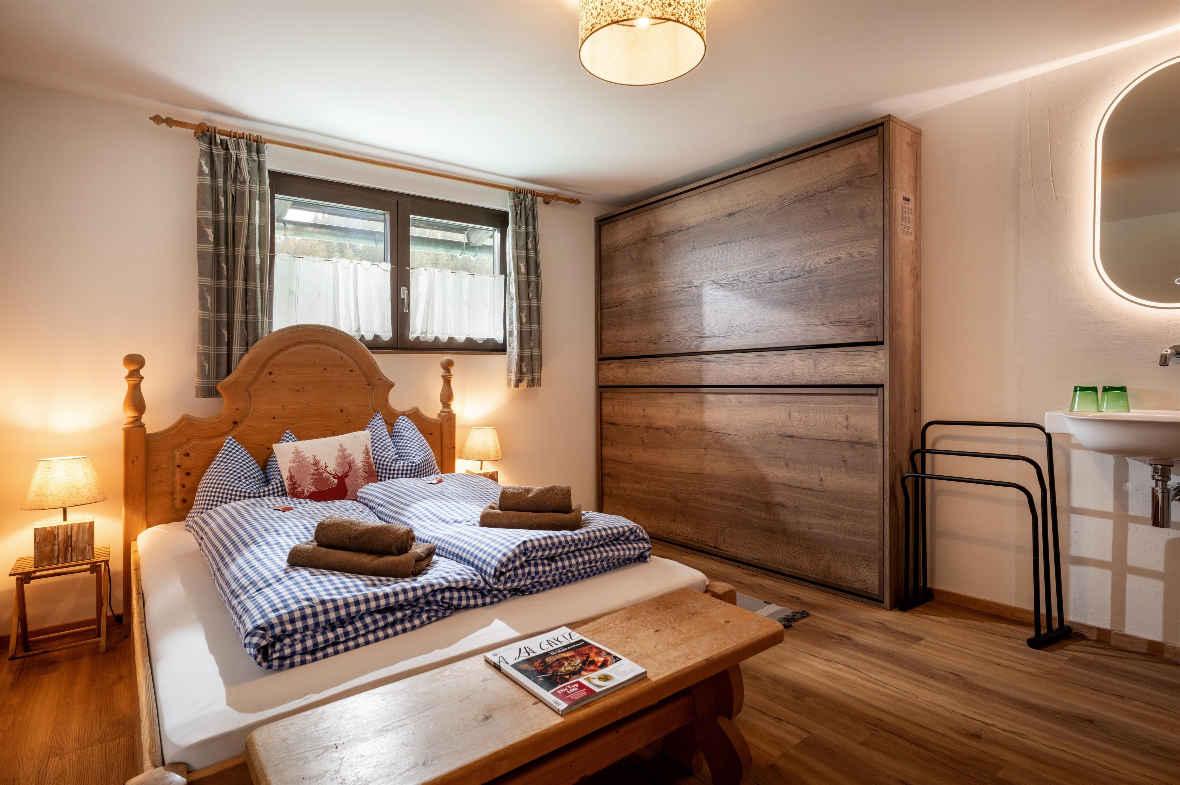 A cozy bedroom with a large bed and wooden details. The warm colors and natural light create an inviting atmosphere.