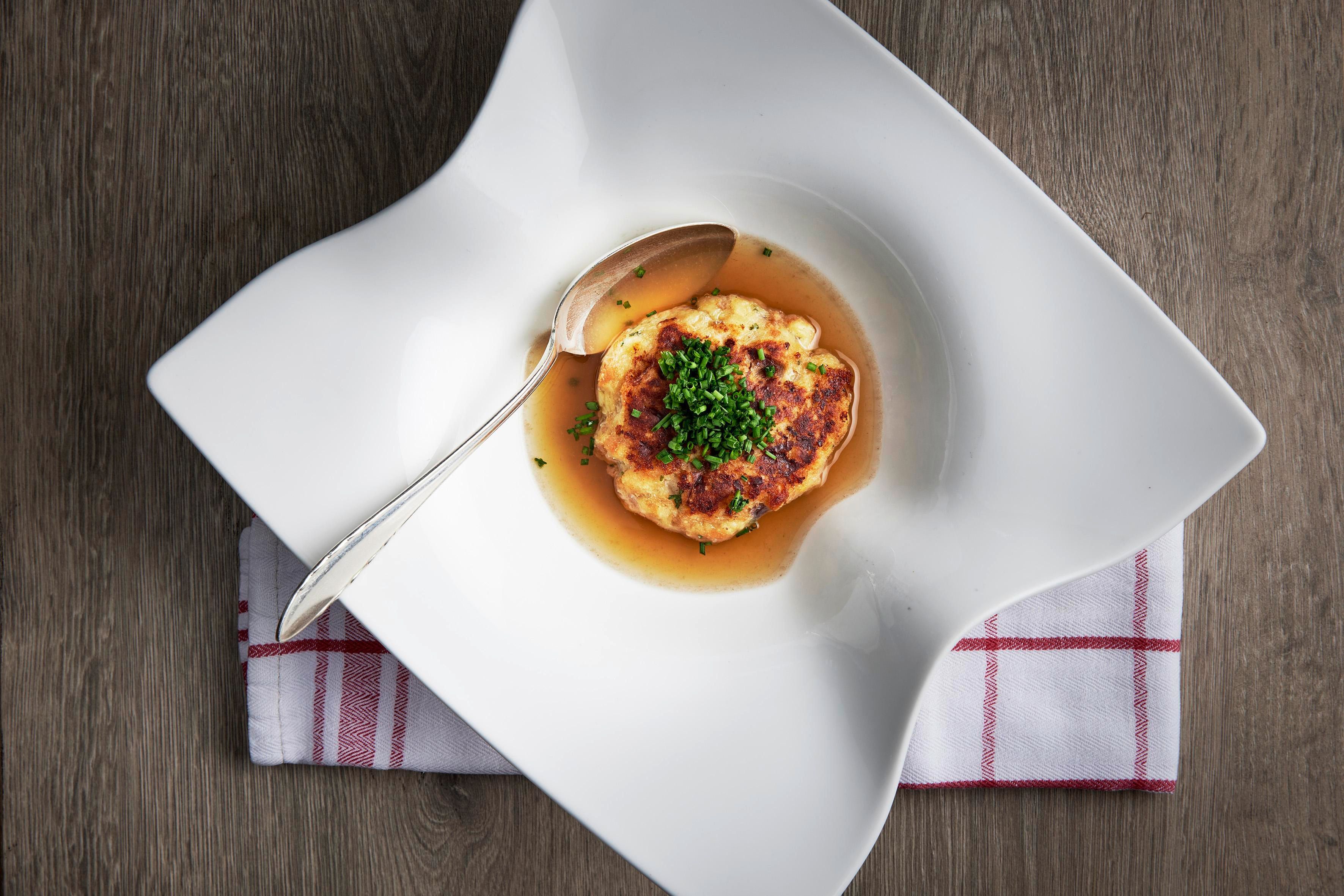 An artistically arranged dish on an elegant plate. It contains a serving, garnished with fresh chives, in a broth.