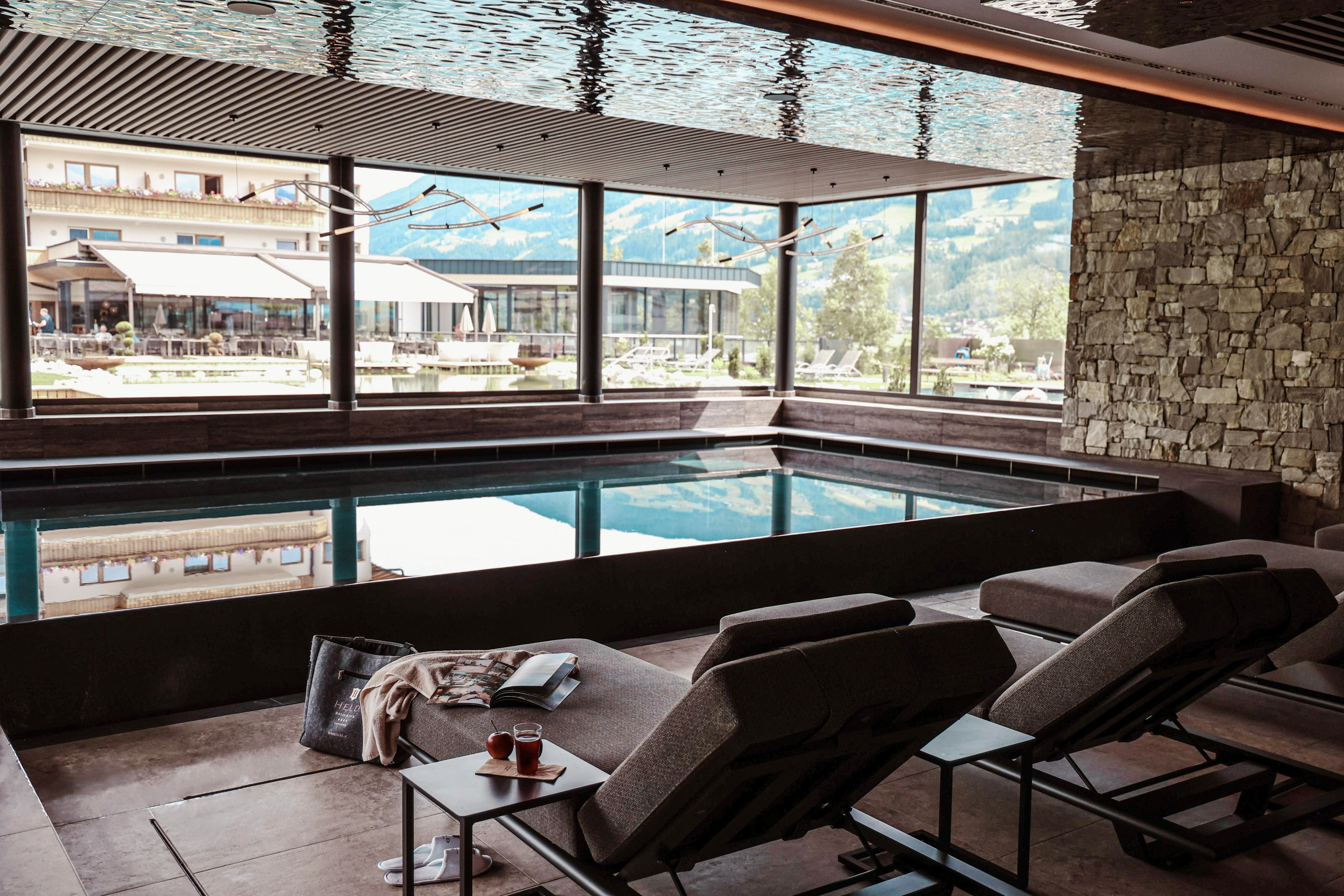 An elegant indoor pool area with comfortable loungers and large windows that provide a view of the surroundings. The space exudes calm and relaxation.
