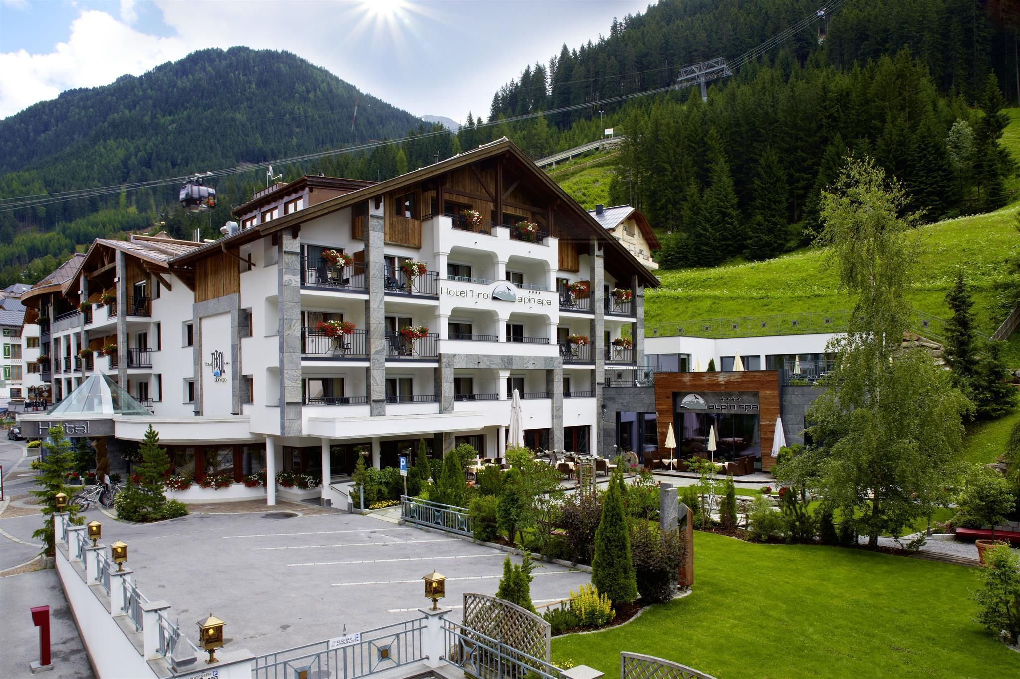 A modern hotel in the mountains with green grass and beautiful trees. In the background, the landscape and the mountains can be seen.
