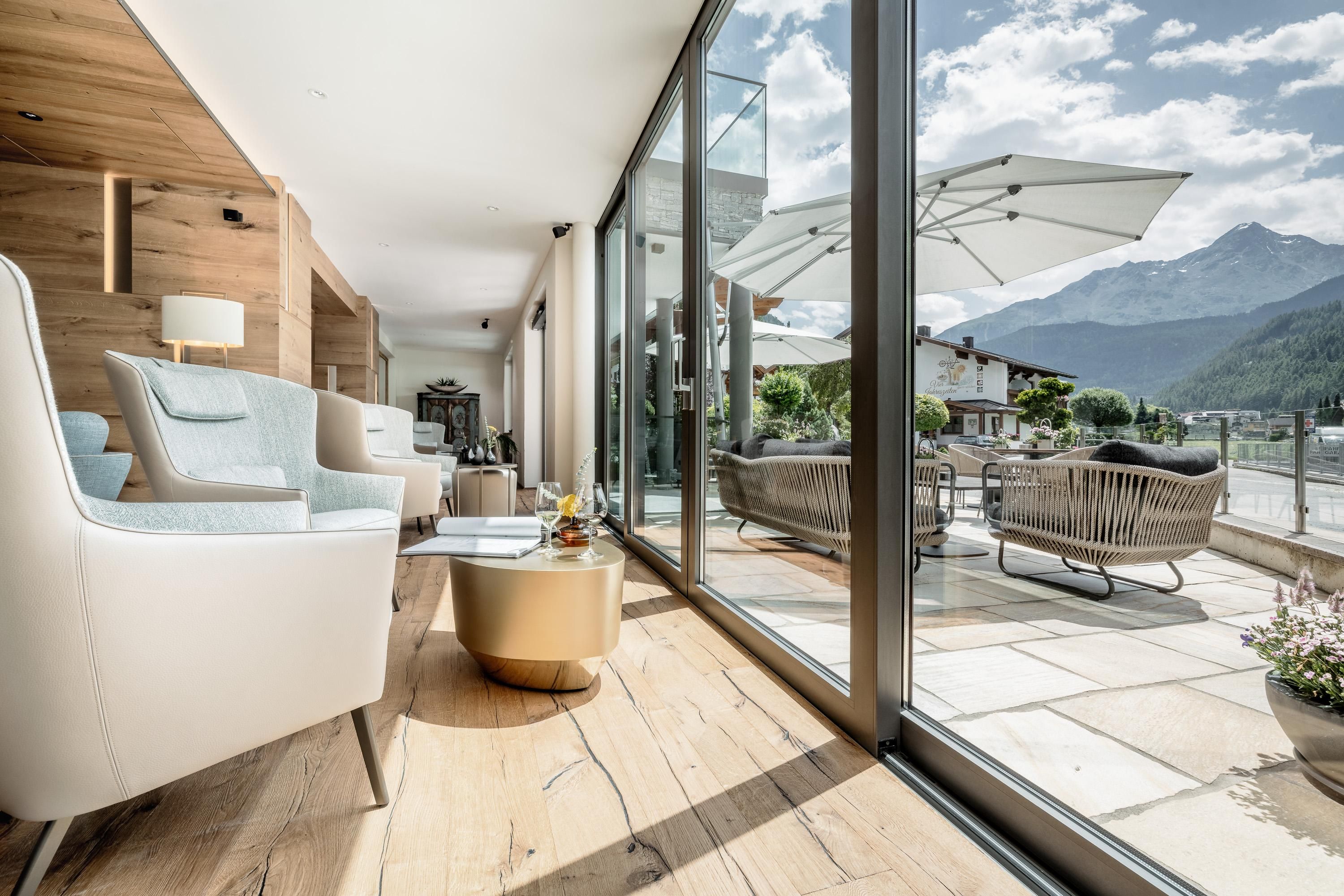 A modern living room with large windows and a magnificent view of the mountains. Outside, there is a cozy terrace with seating and a sunshade.