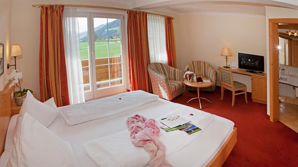 A cozy hotel room with a large bed and a seating area. Large windows offer a view of the landscape.