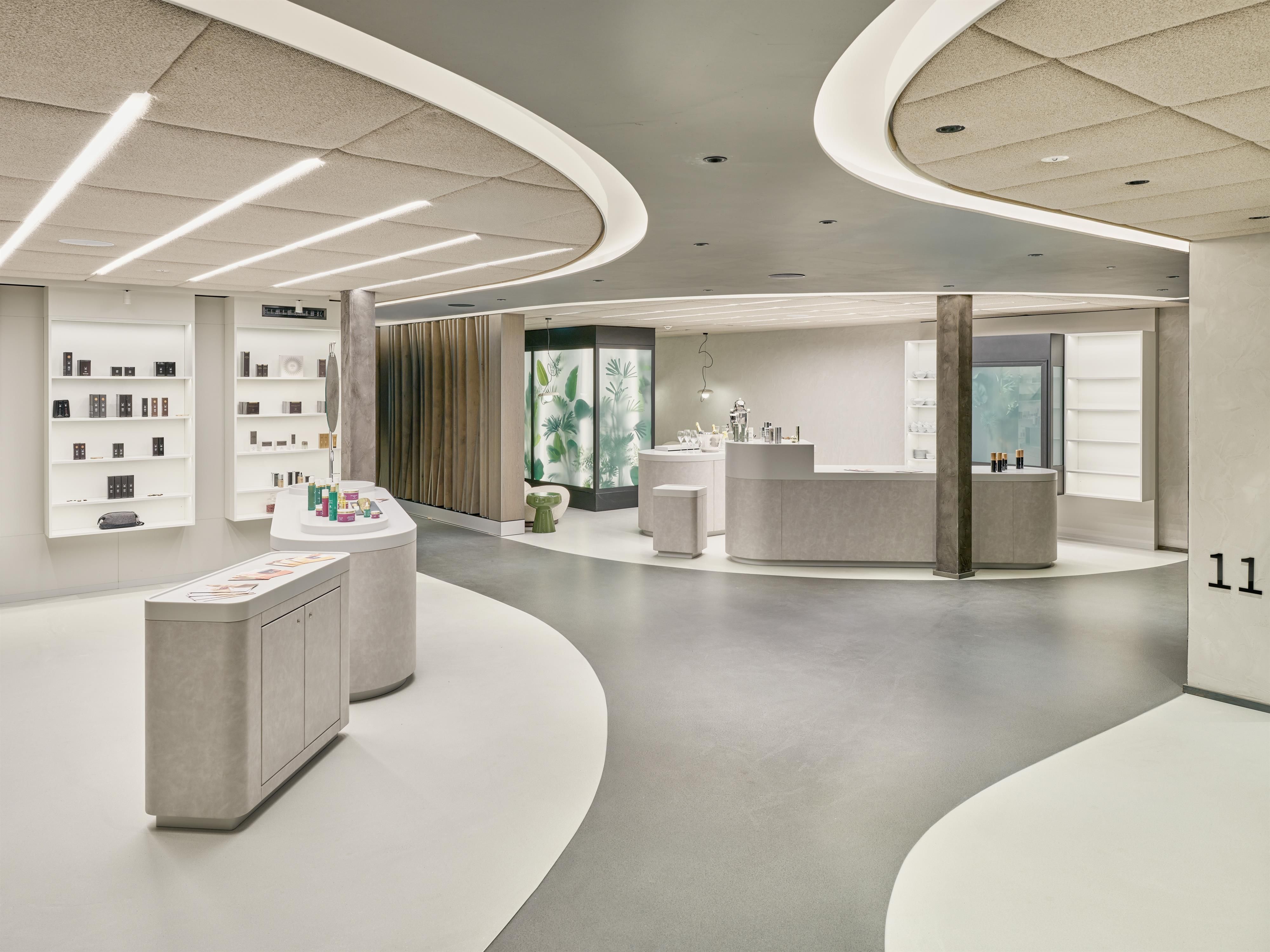 A modern sales room with curved walls and bright light. Products are displayed on the walls, and in the background, there is a window with a view outside.