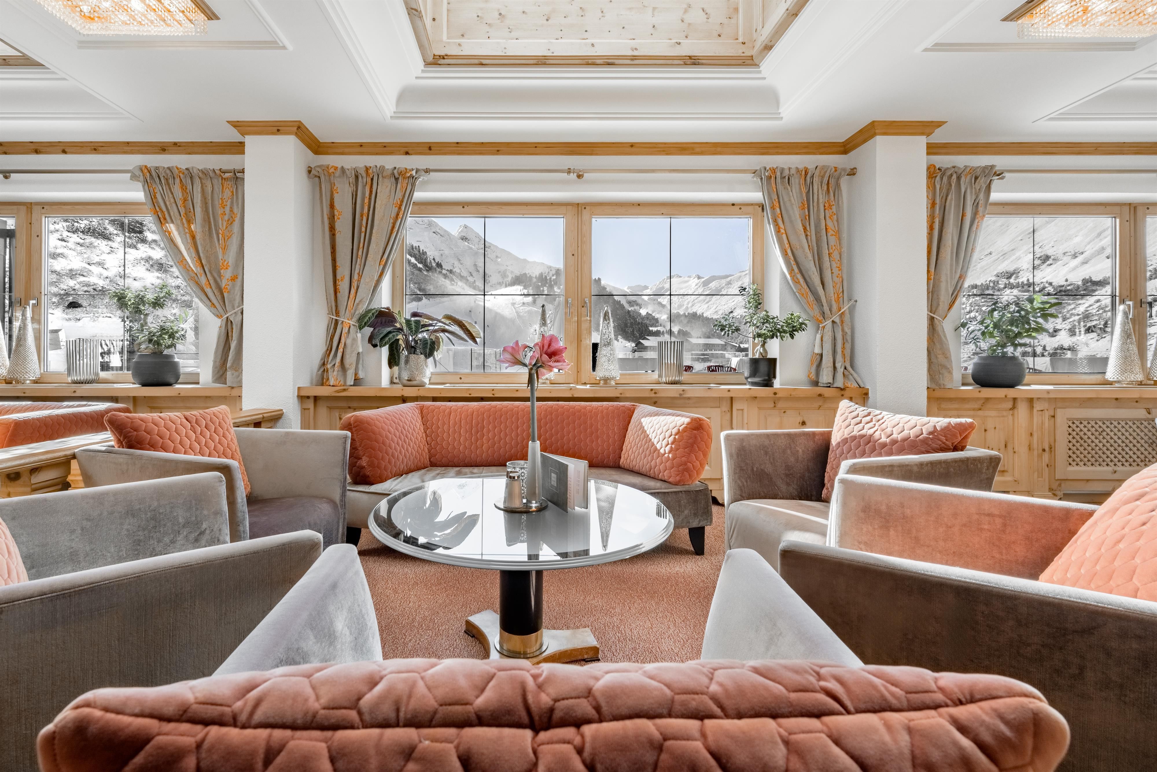 An elegant living area with cozy sofas and a central table. Large windows let in plenty of light and offer a view of the mountains.