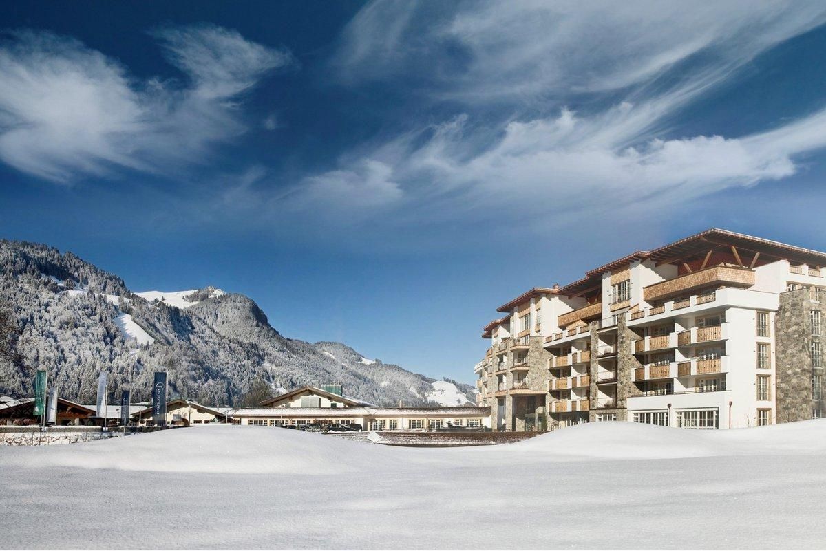A modern hotel building in a snowy landscape. In the background, majestic mountains and a clear blue sky can be seen.