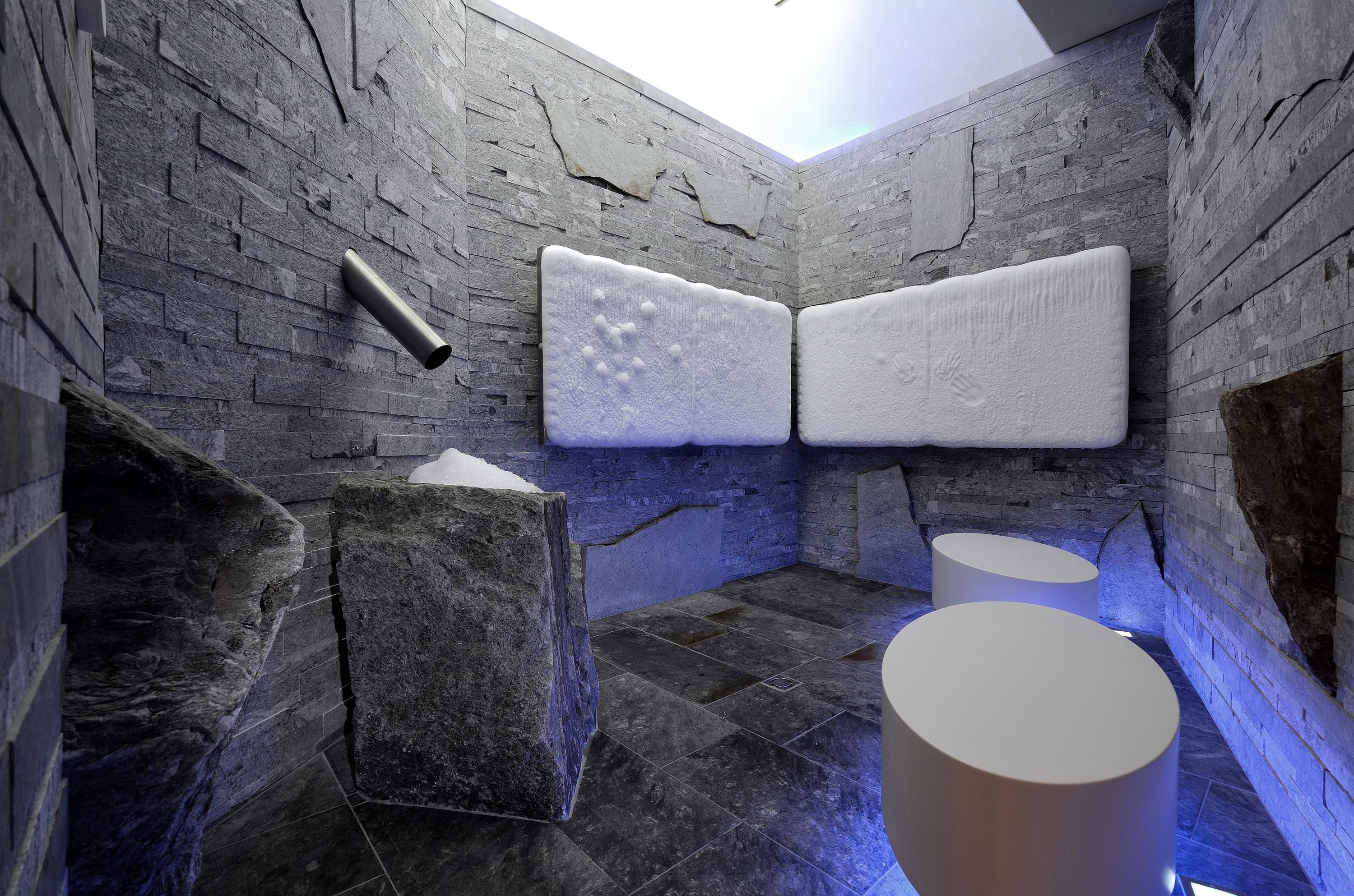 A modern room with gray stones and white walls. There are round stools and a relaxing atmosphere.