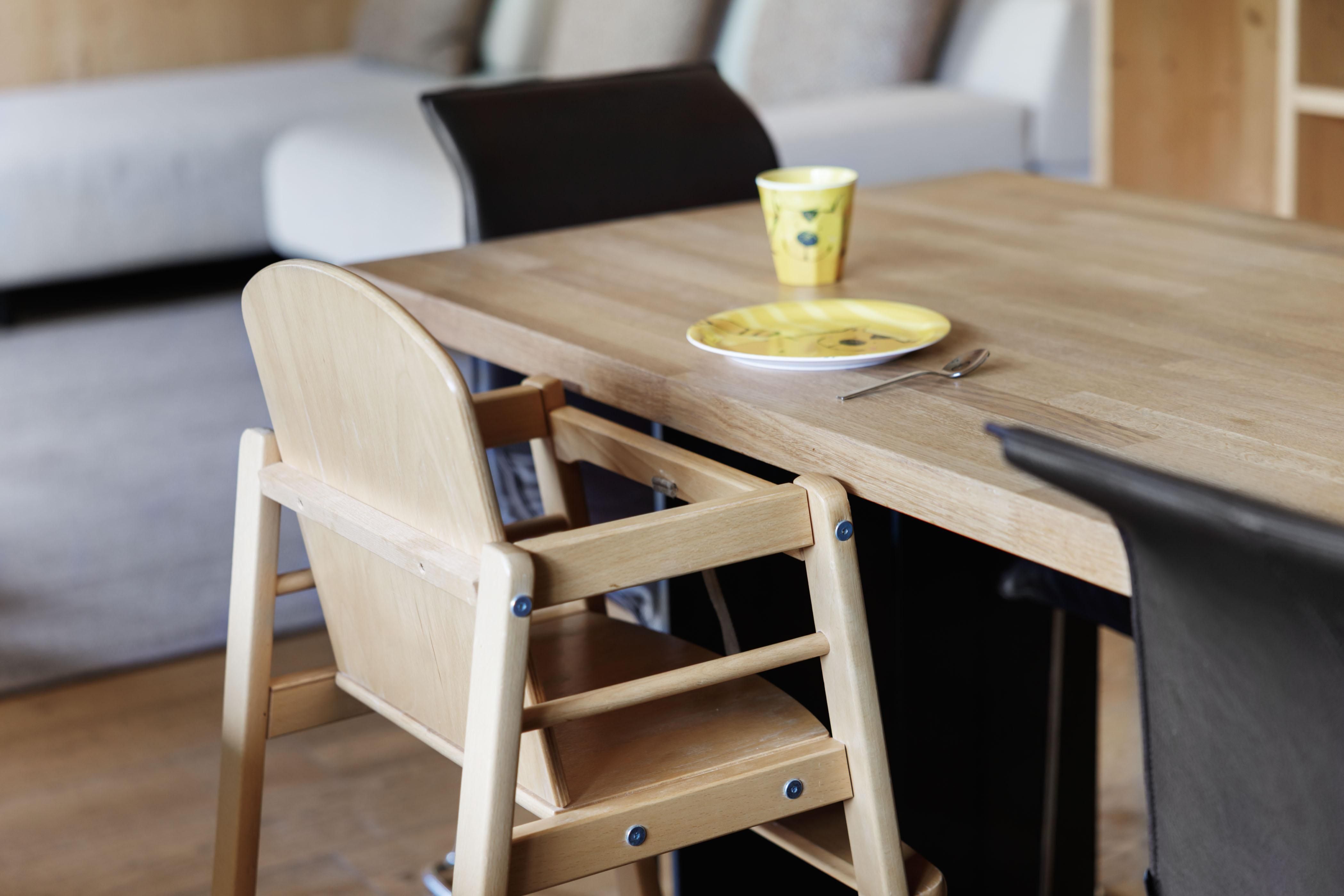 A dining area with a wooden high chair. On the table is a yellow cup and a plate.