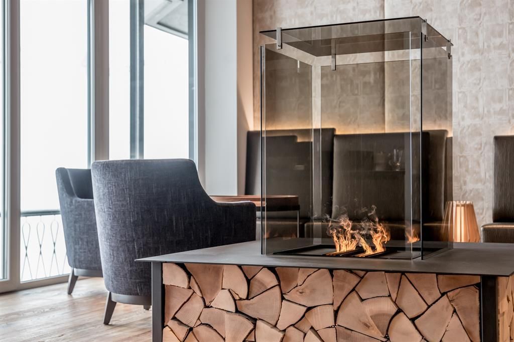 An elegant living space with a modern glass fireplace and wood storage. Two comfortable armchairs create a cozy atmosphere.