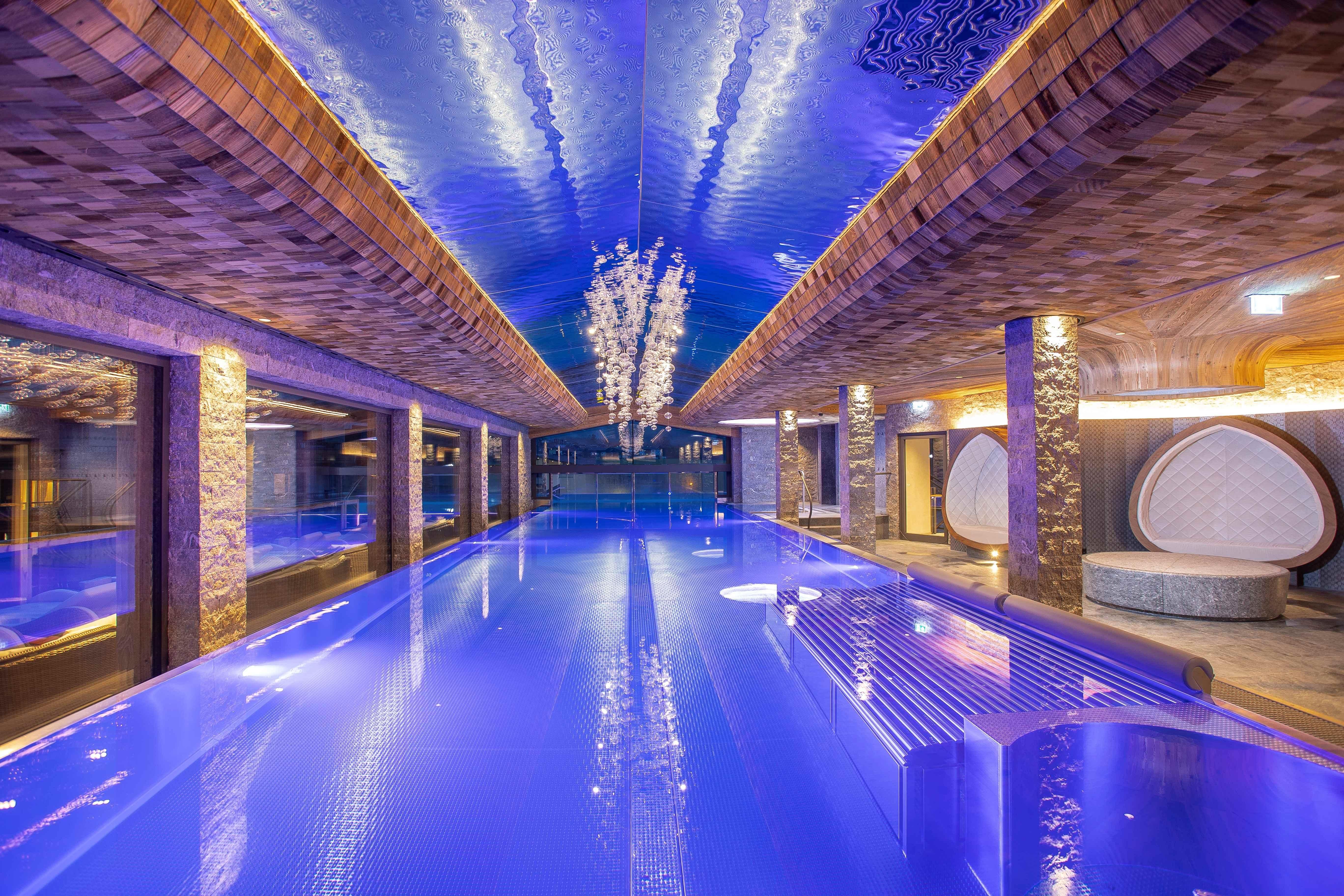 A luxurious indoor pool with blue water and stylish lighting. The walls are designed with modern materials, creating a relaxing atmosphere.