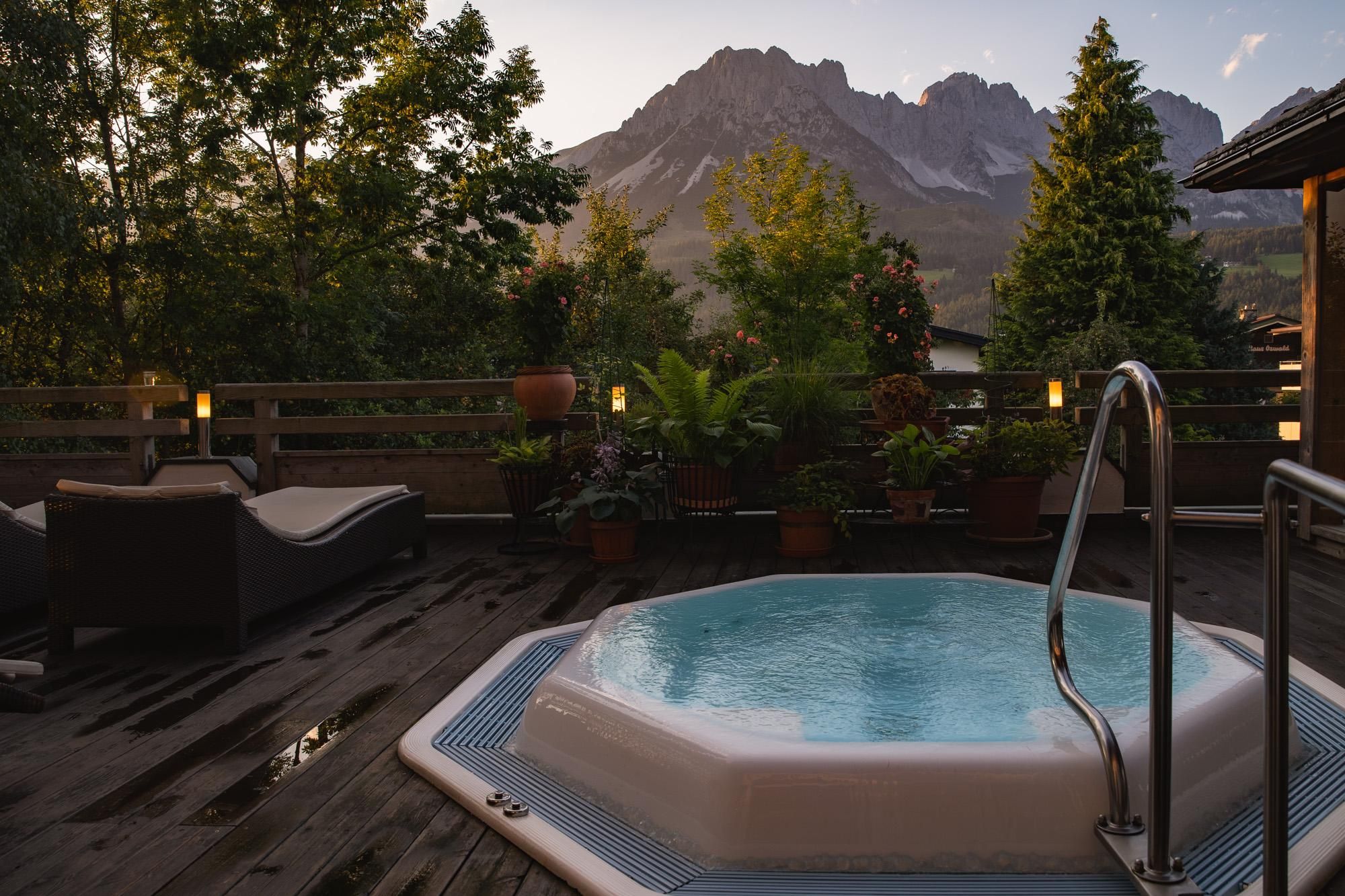A hot tub on a terrace with a view of the mountains. Green plants and cozy loungers complete the relaxing atmosphere.