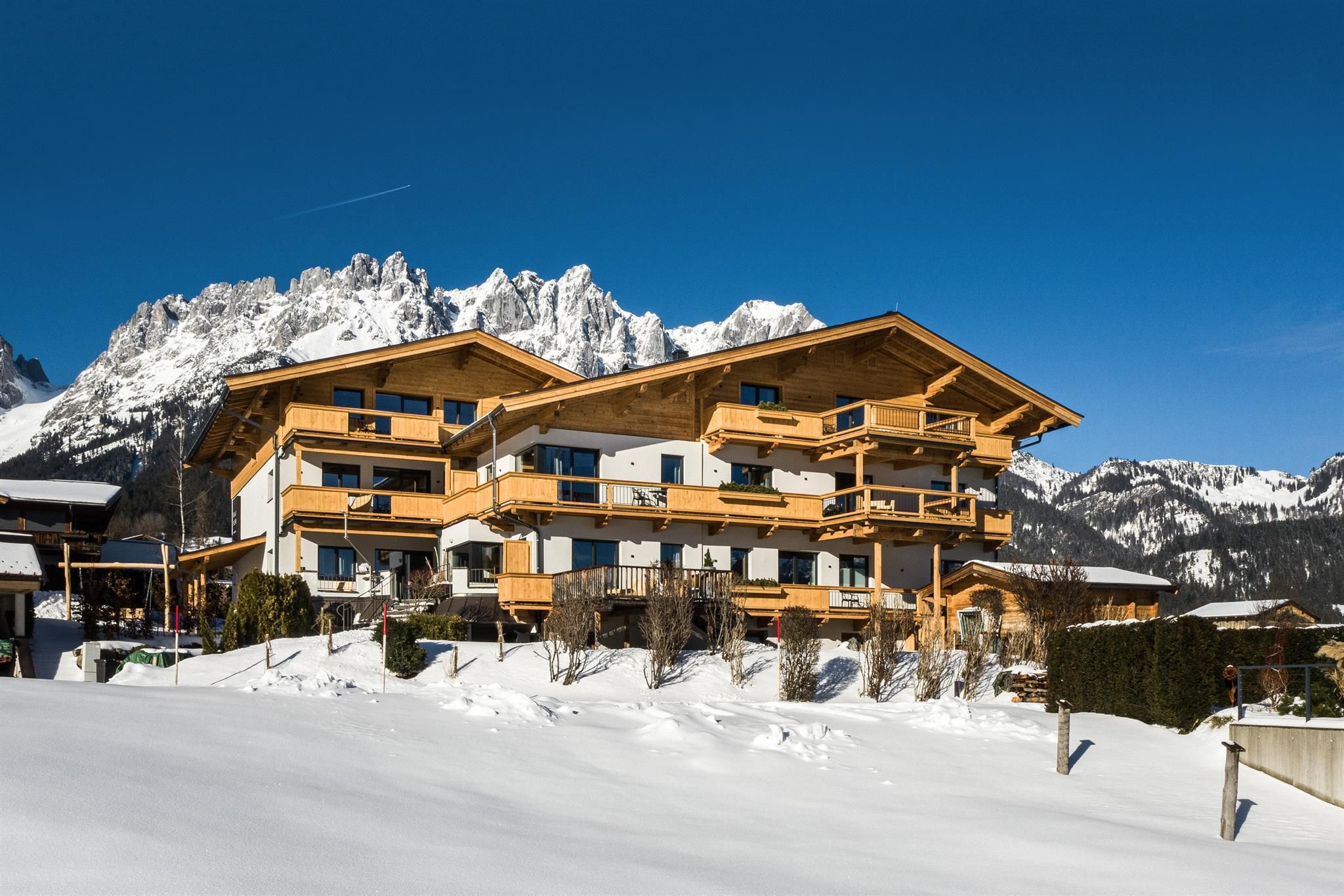 A modern chalet in the snow with a view of the mountains. The clear blue sky complements the winter landscape.
