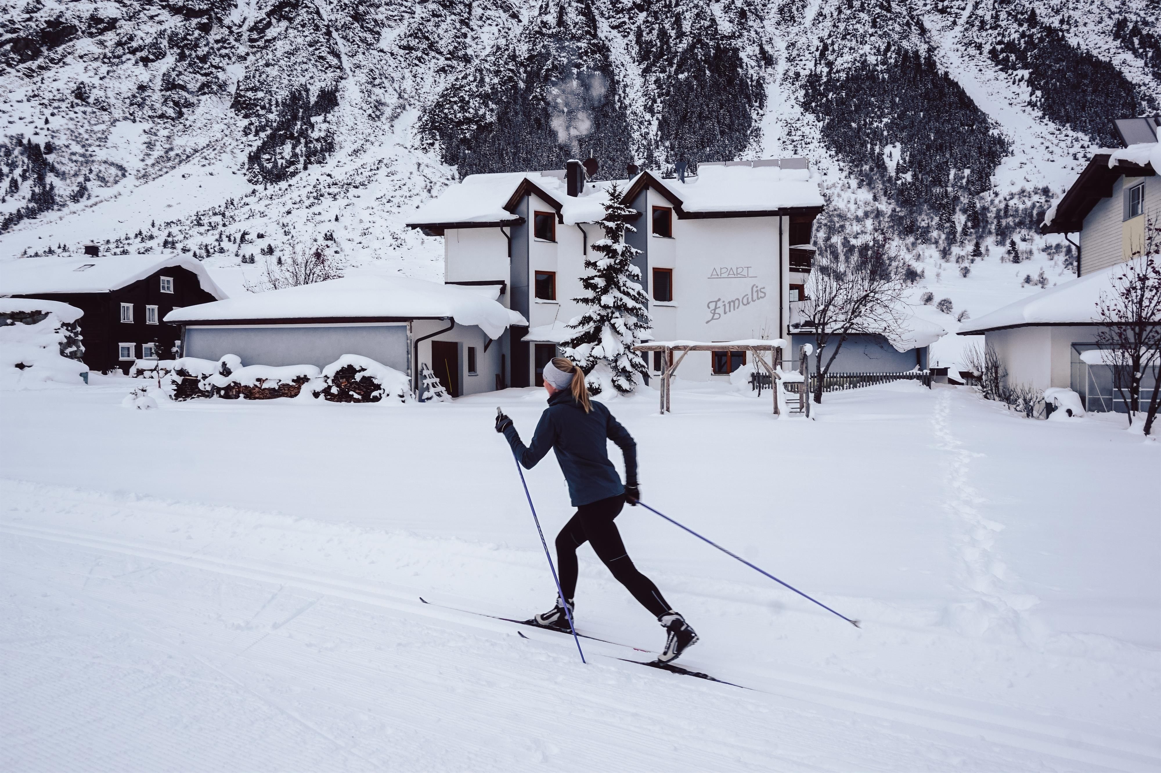 A person is skiing through a snowy landscape. In the background, beautiful mountain houses and a winter landscape can be seen.