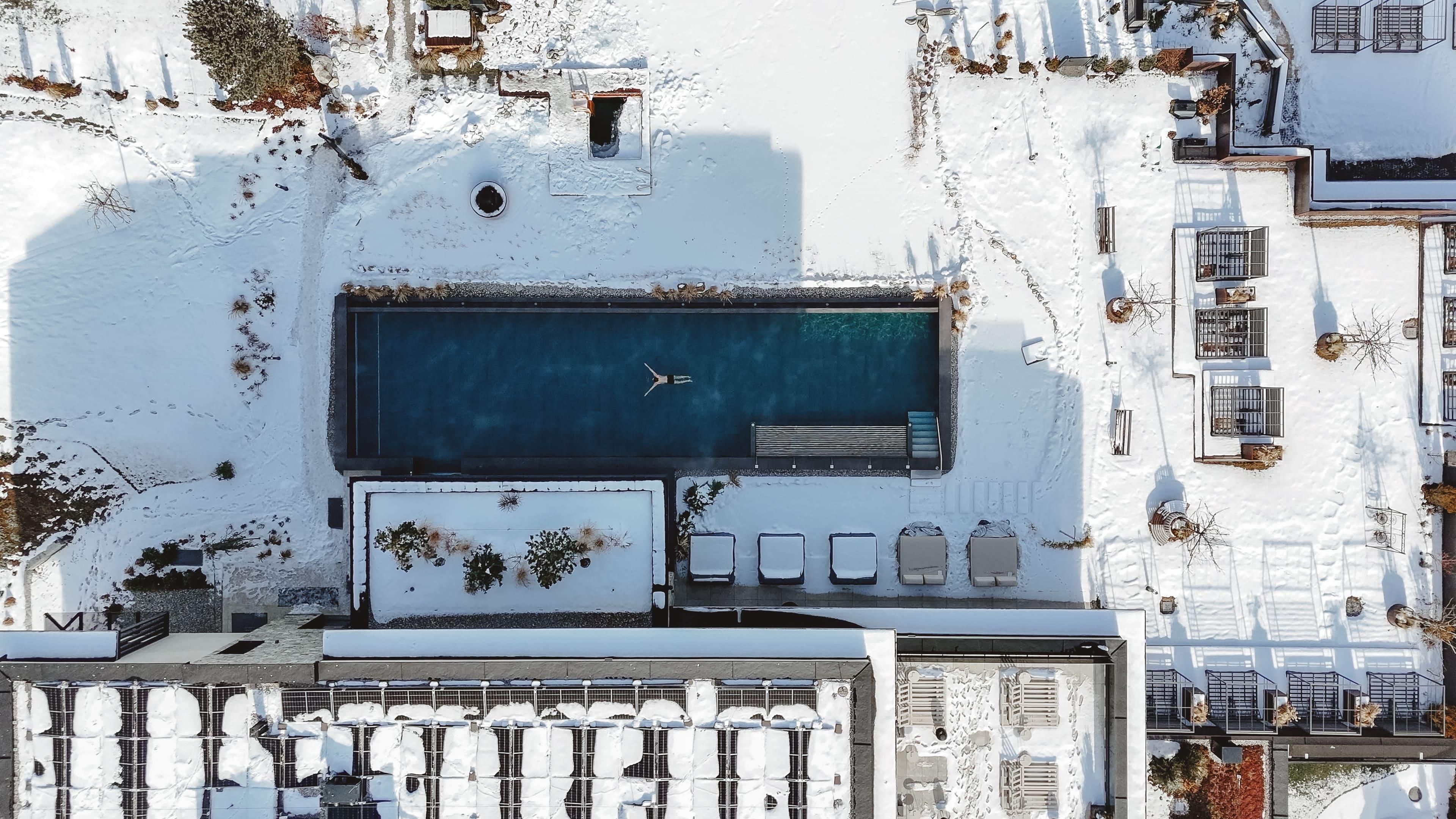 A swimming pool is idyllically located in the snow, surrounded by white areas. Some loungers are arranged next to the pool.