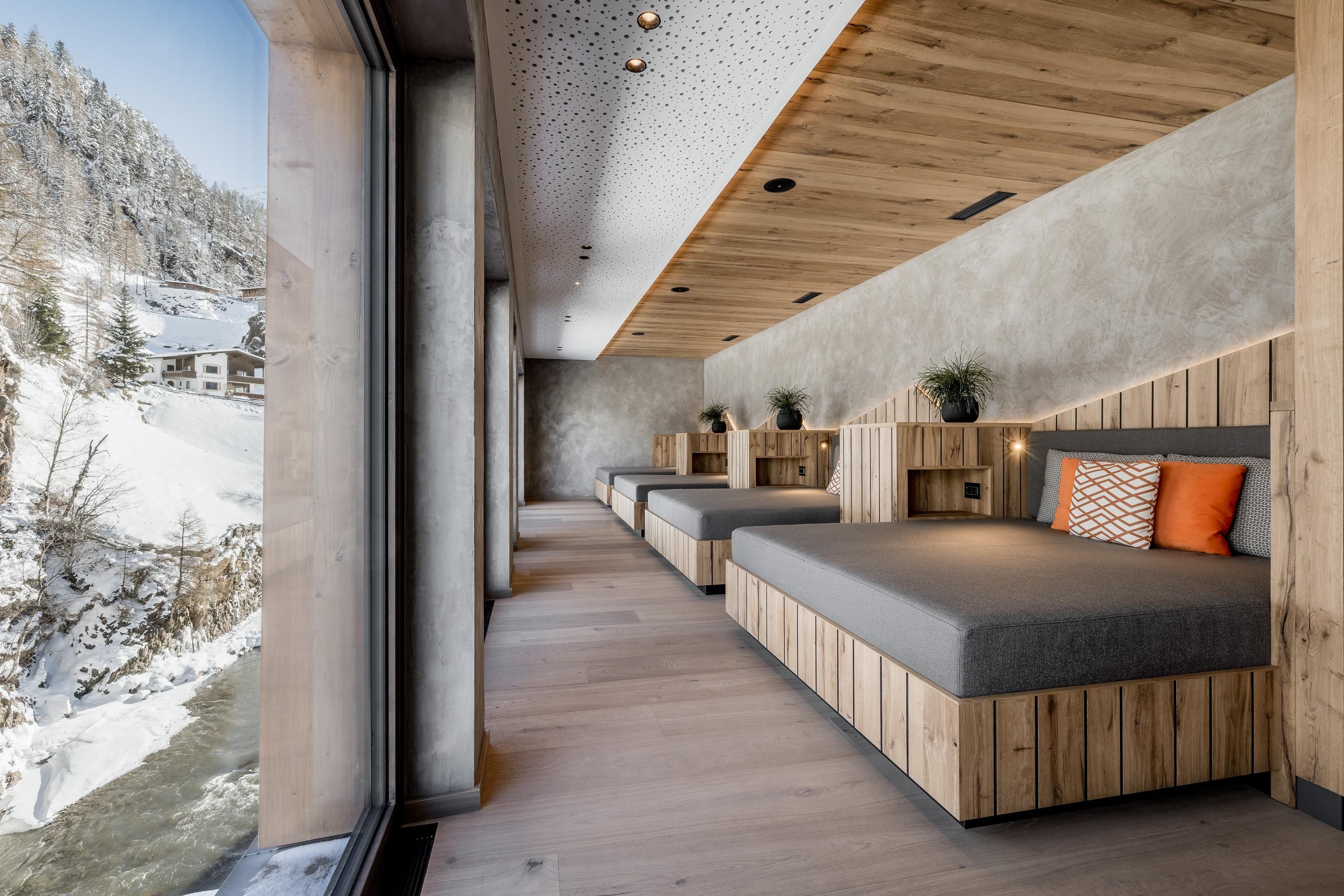 A modern room with wood and concrete elements. Large windows offer a view of the snow-covered landscape.