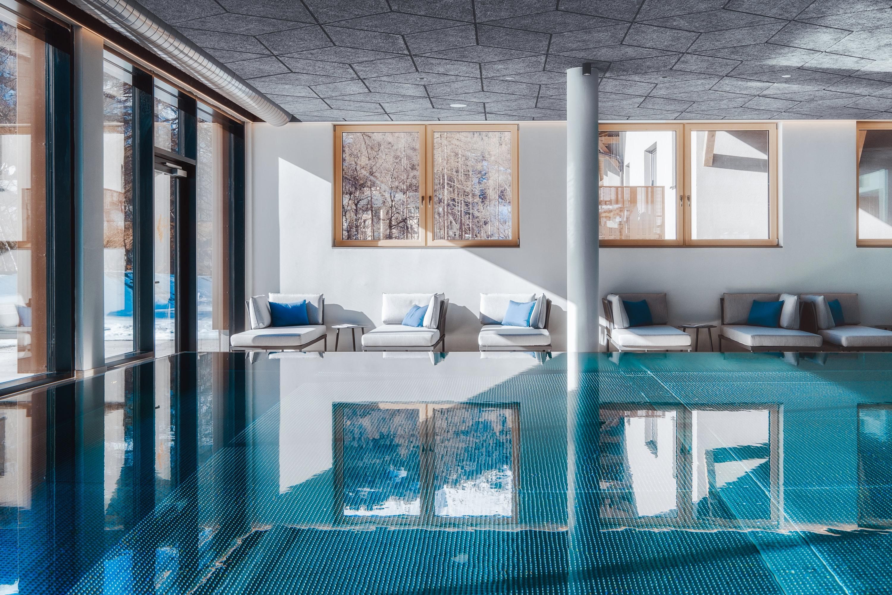 An elegant wellness area with a clear water pool and comfortable loungers. Large windows provide plenty of natural light and a relaxed atmosphere.