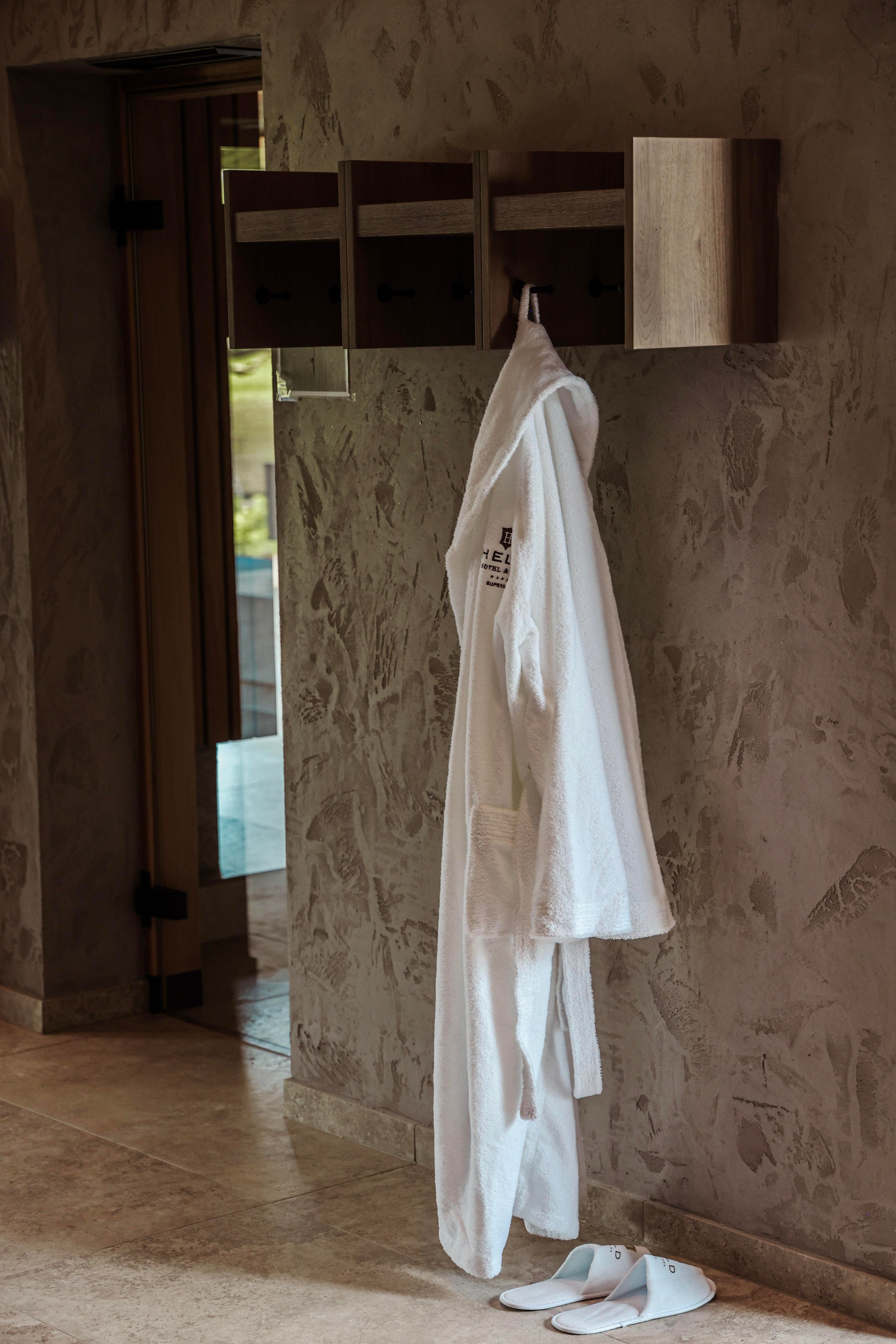 A white bathrobe hangs on a wooden board with compartments. The background features a stylish interior design.