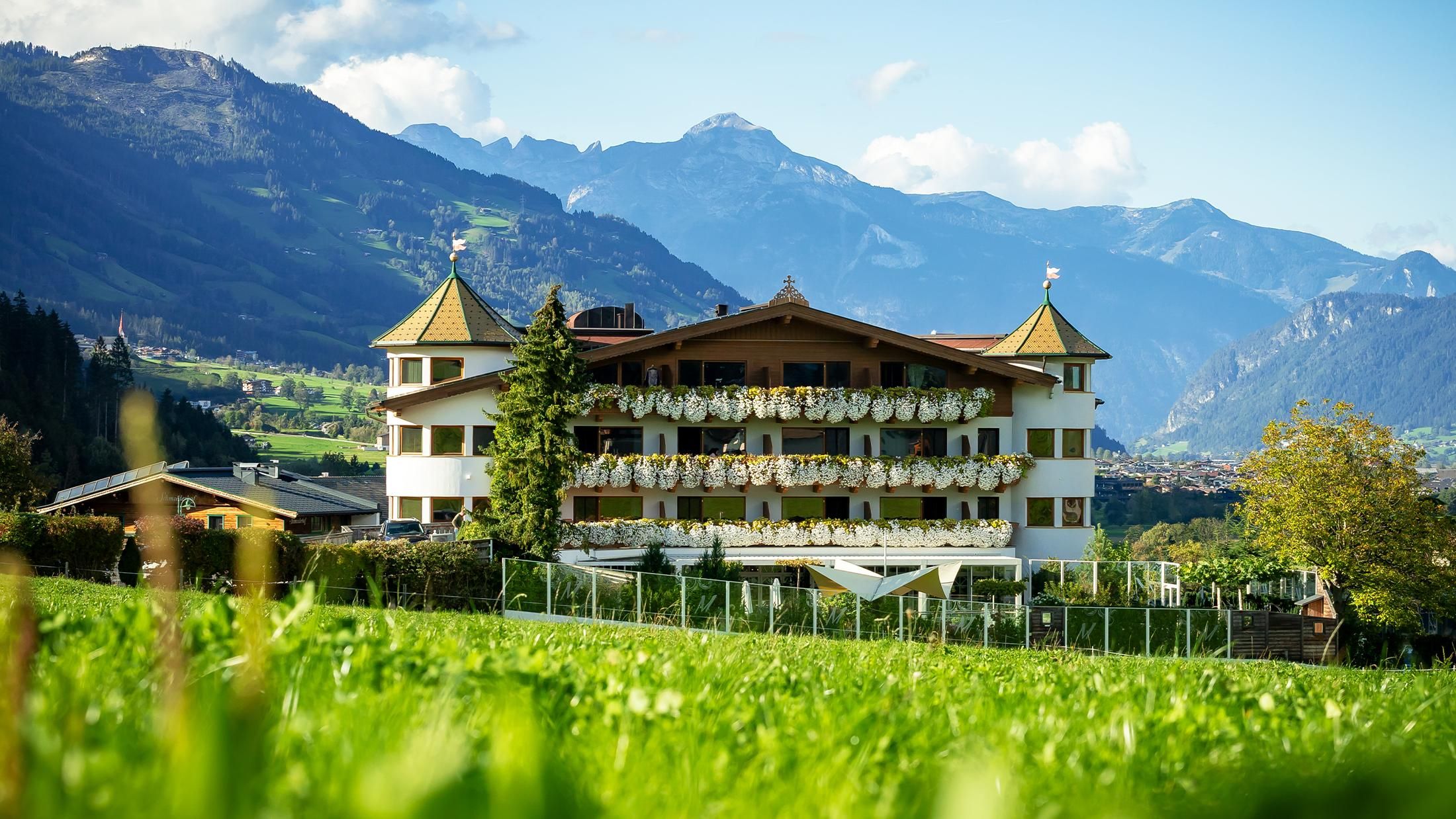 A picturesque building in alpine style, surrounded by green meadows and mountains. The sky is clear and displays a peaceful landscape.
