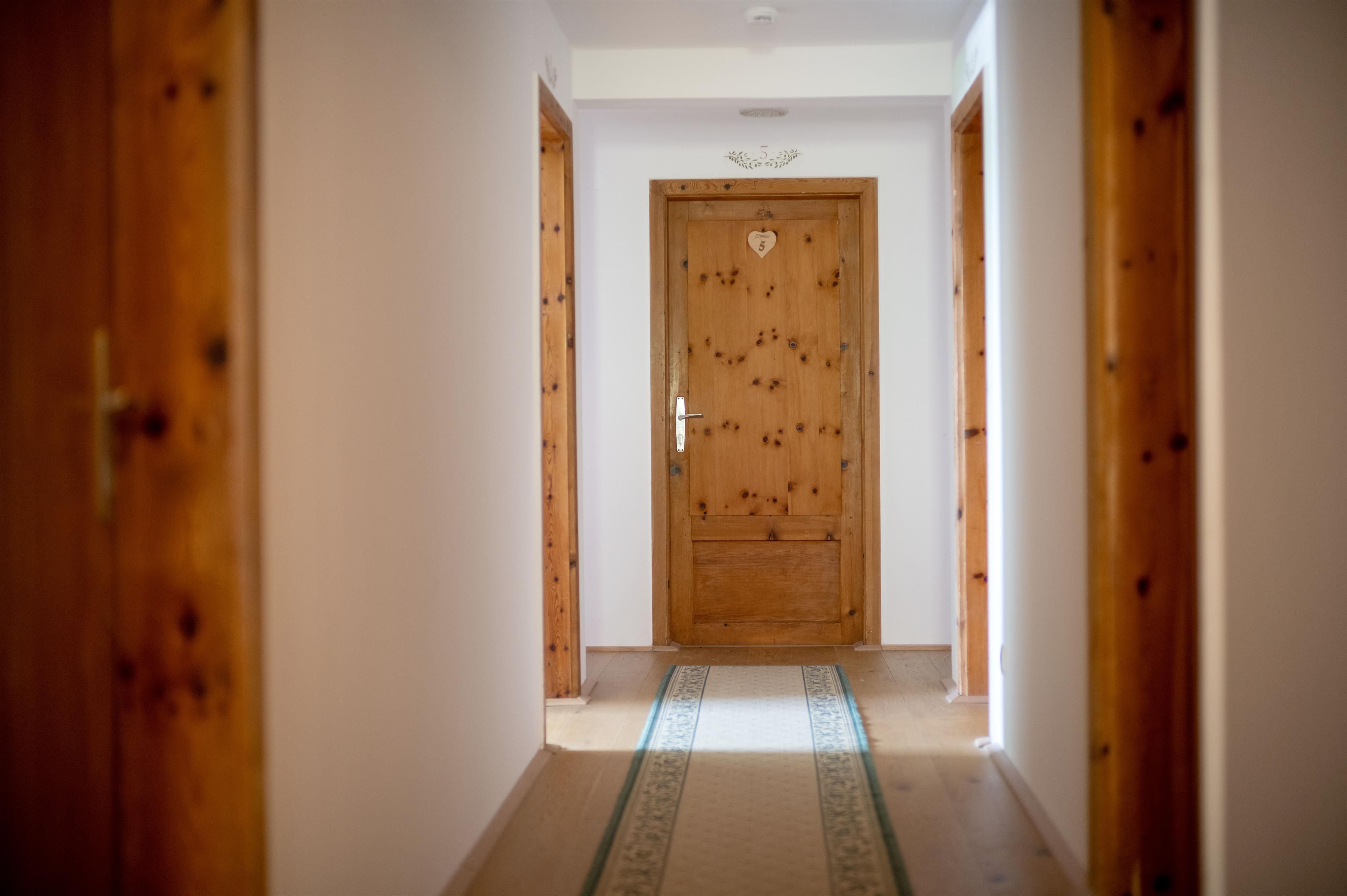 A bright hallway with wooden doors and a carpet in the middle. The walls are white and the atmosphere is welcoming.