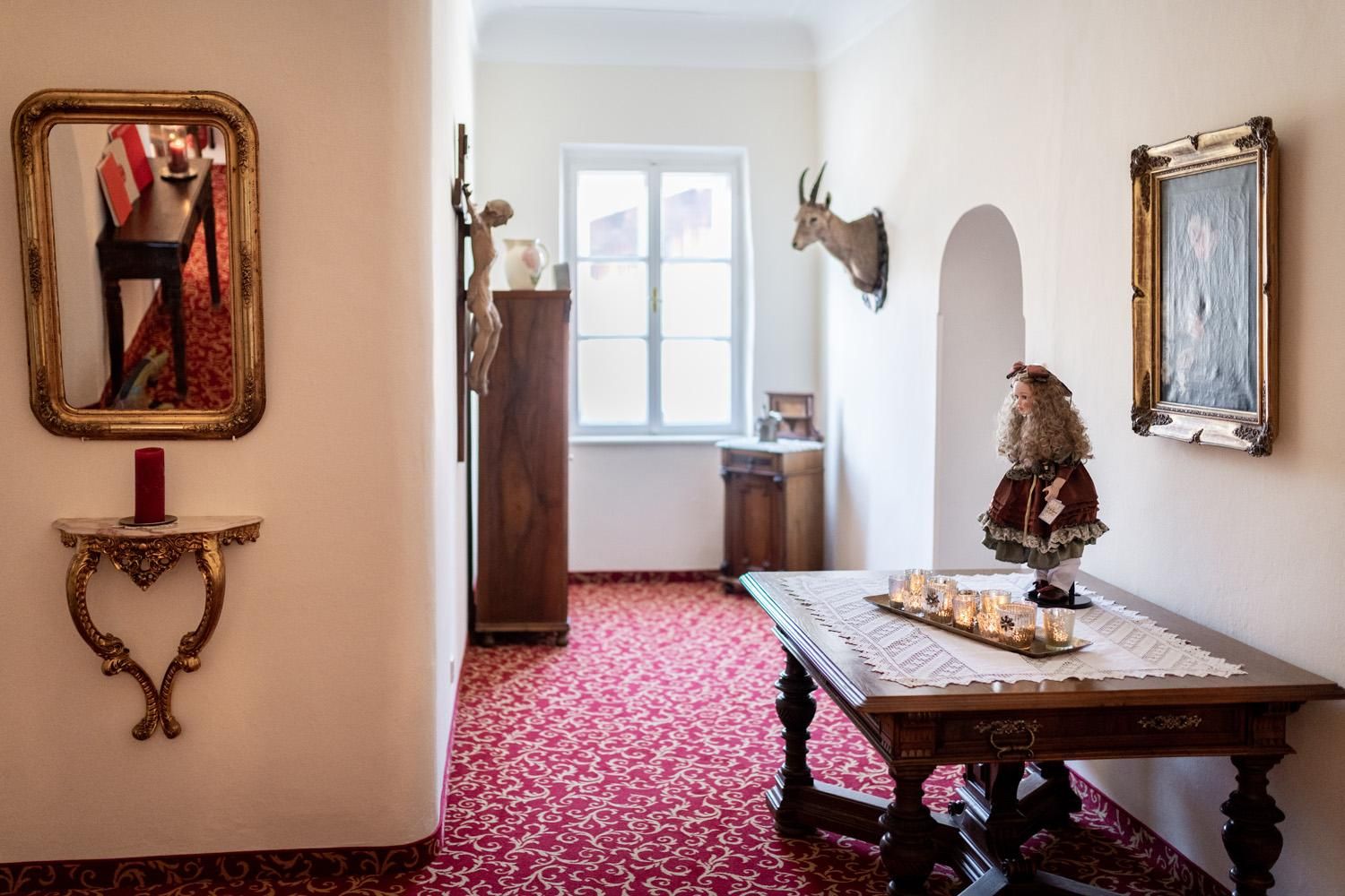 An elegant hallway with a red carpet and white walls. On a table, there is a decorative figure and candles.