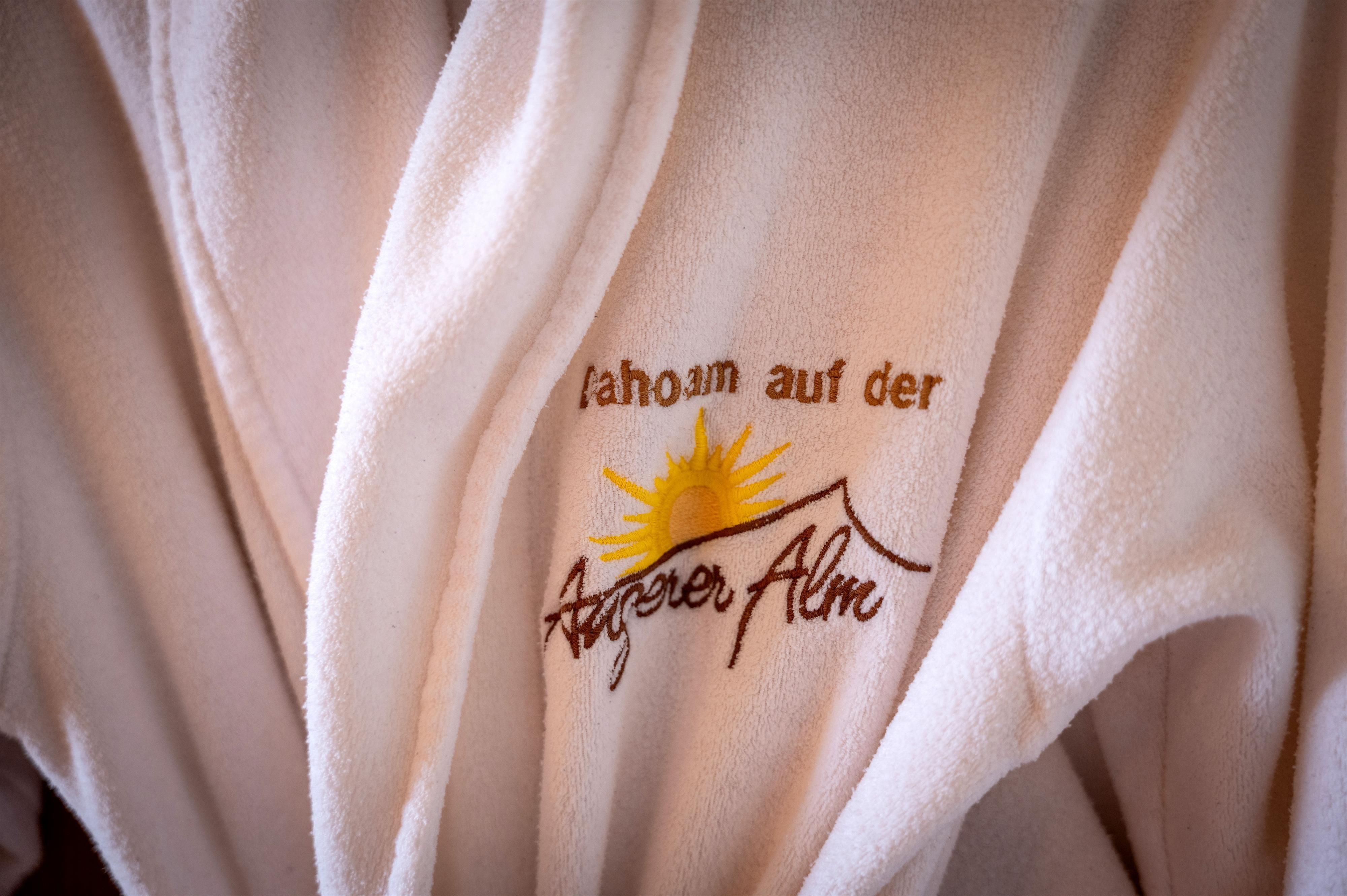 A soft bathrobe with the print "Home on the Angerer Alm" and a sunny graphic. The bathrobe conveys a feeling of coziness and relaxation.