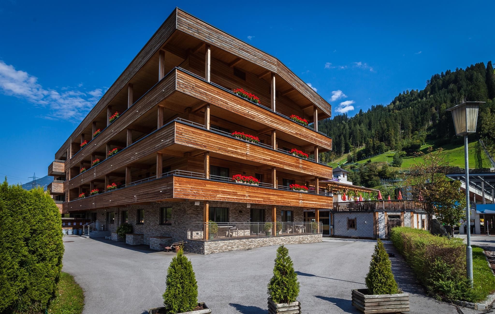 A modern wooden building in the mountains with several floors. The clear sky and the surrounding nature create a beautiful atmosphere.