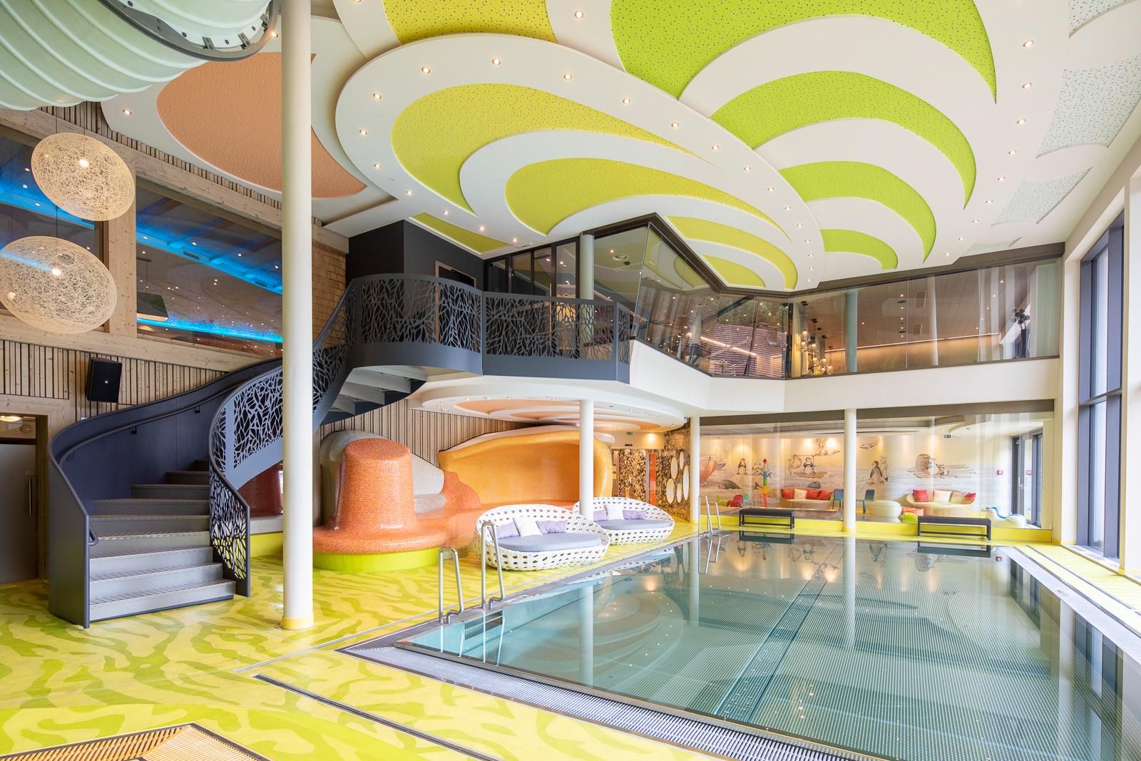 A modern interior with a pool and colorful, curved ceilings. The environment is bright and inviting, with a stylish staircase and cozy seating areas.