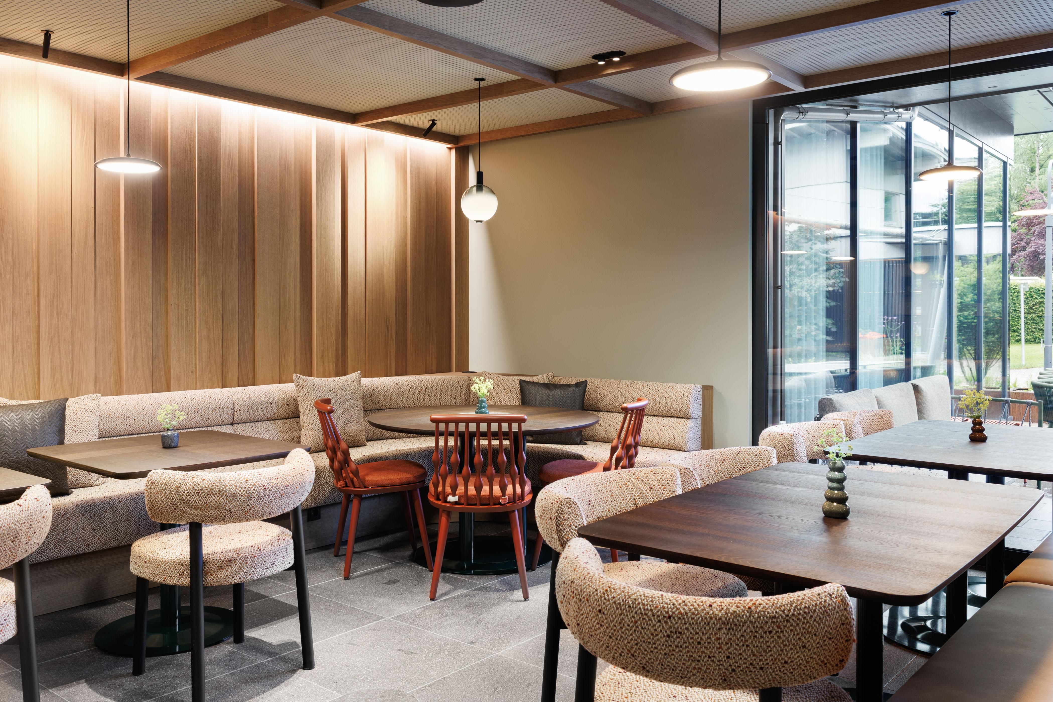 A modern café with stylish seating areas and warm wood paneling. Large windows let in plenty of light and offer a view outside.