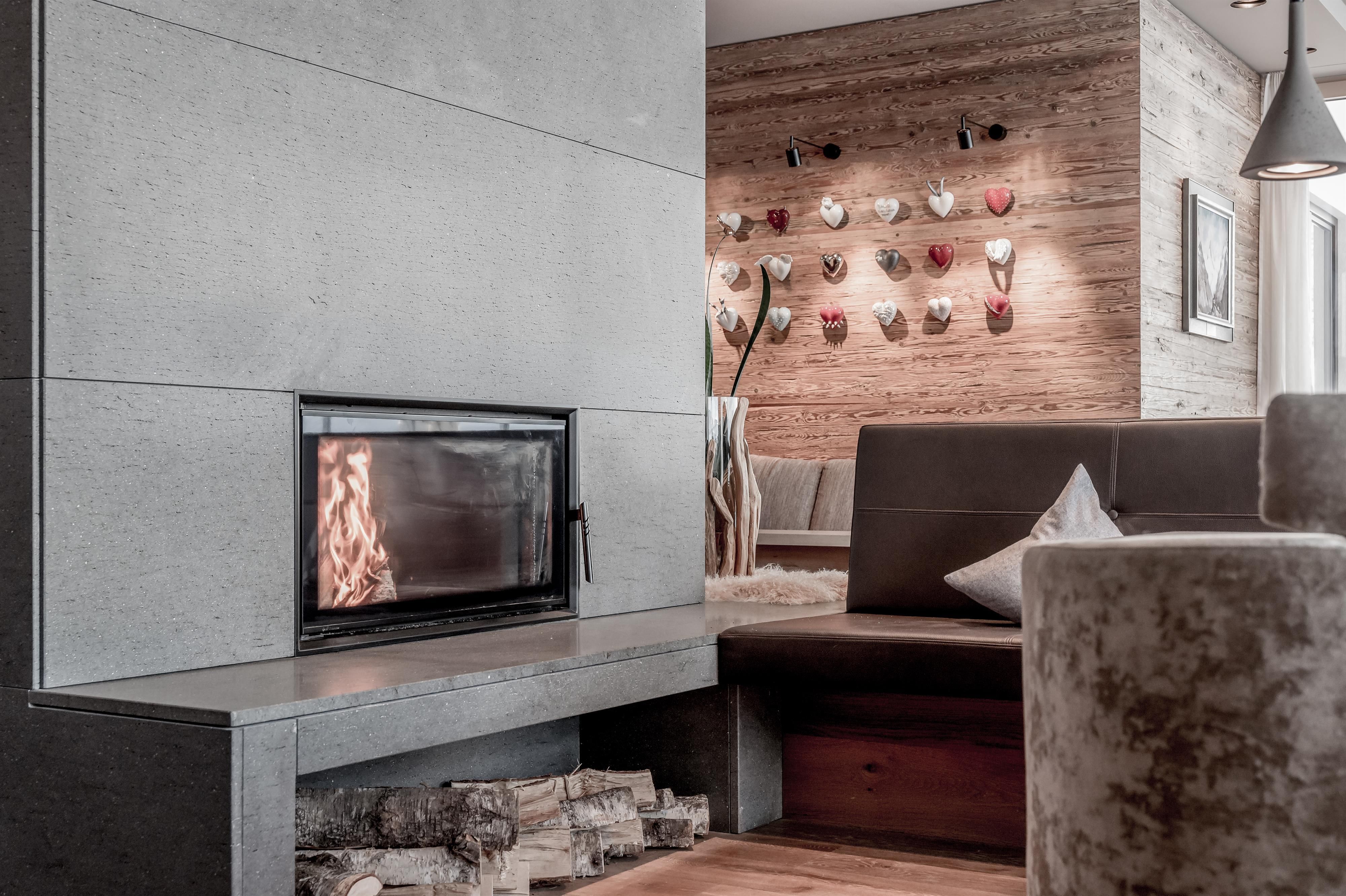 A modern fireplace with an open flame is situated in an elegant living space. In the background, decorative elements on the wall can be seen.