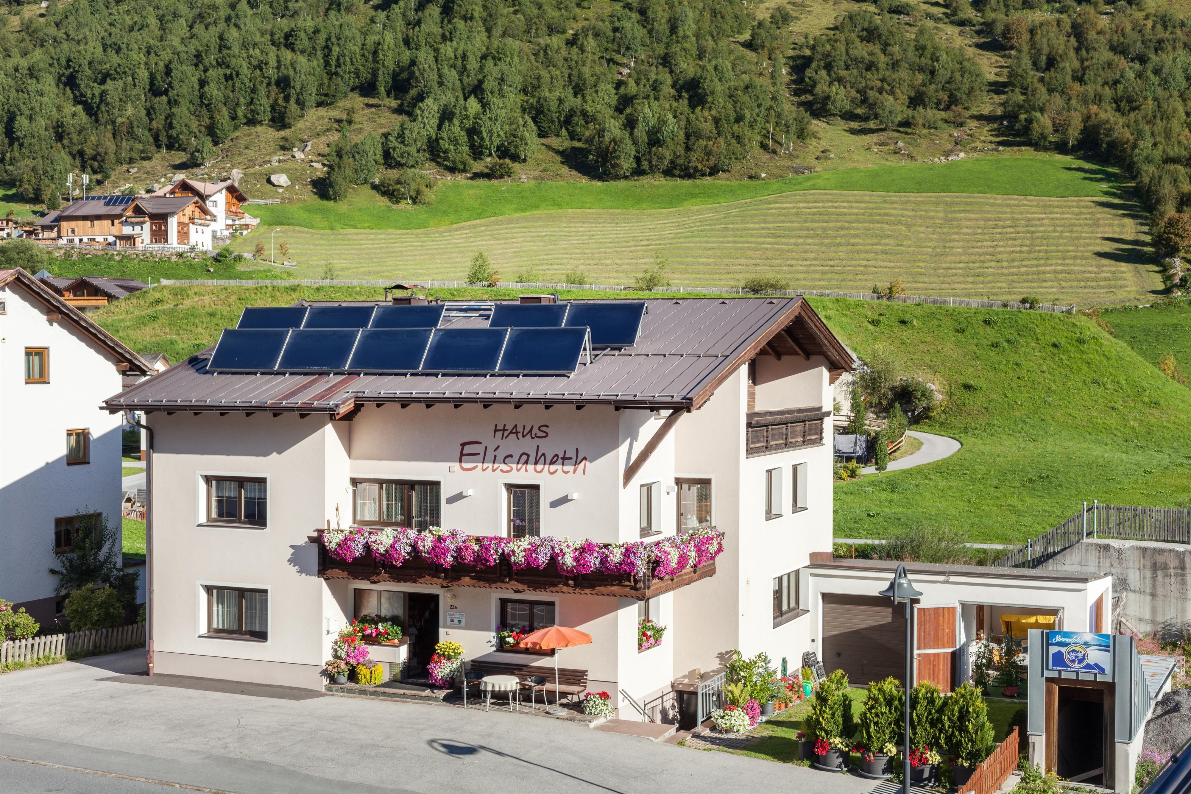 A cozy house with a balcony, adorned with flowers. In the background, green meadows and hills stretch out.