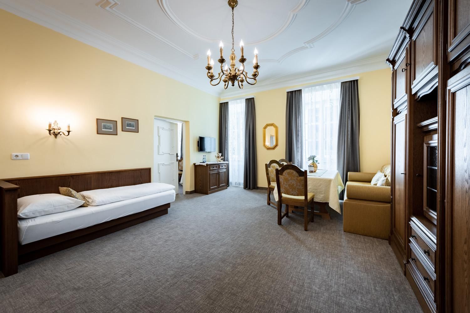 A spacious room with a single bed, a table, and chairs. Large windows let in plenty of light and the decor is classic and cozy.