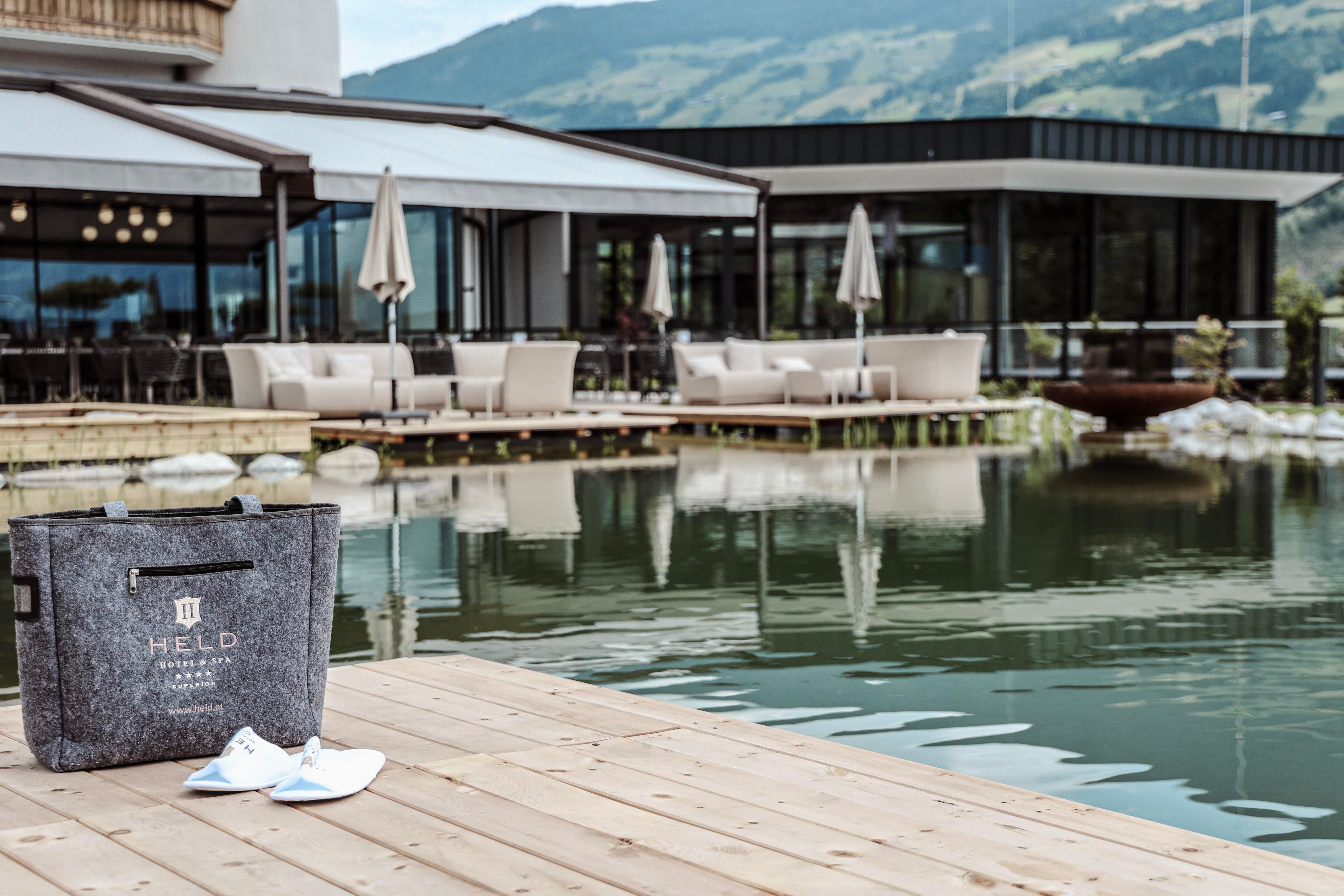 An elegant outdoor area with lounge furniture by the water. In the foreground, there is a bag and a pair of shoes on a wooden walkway.