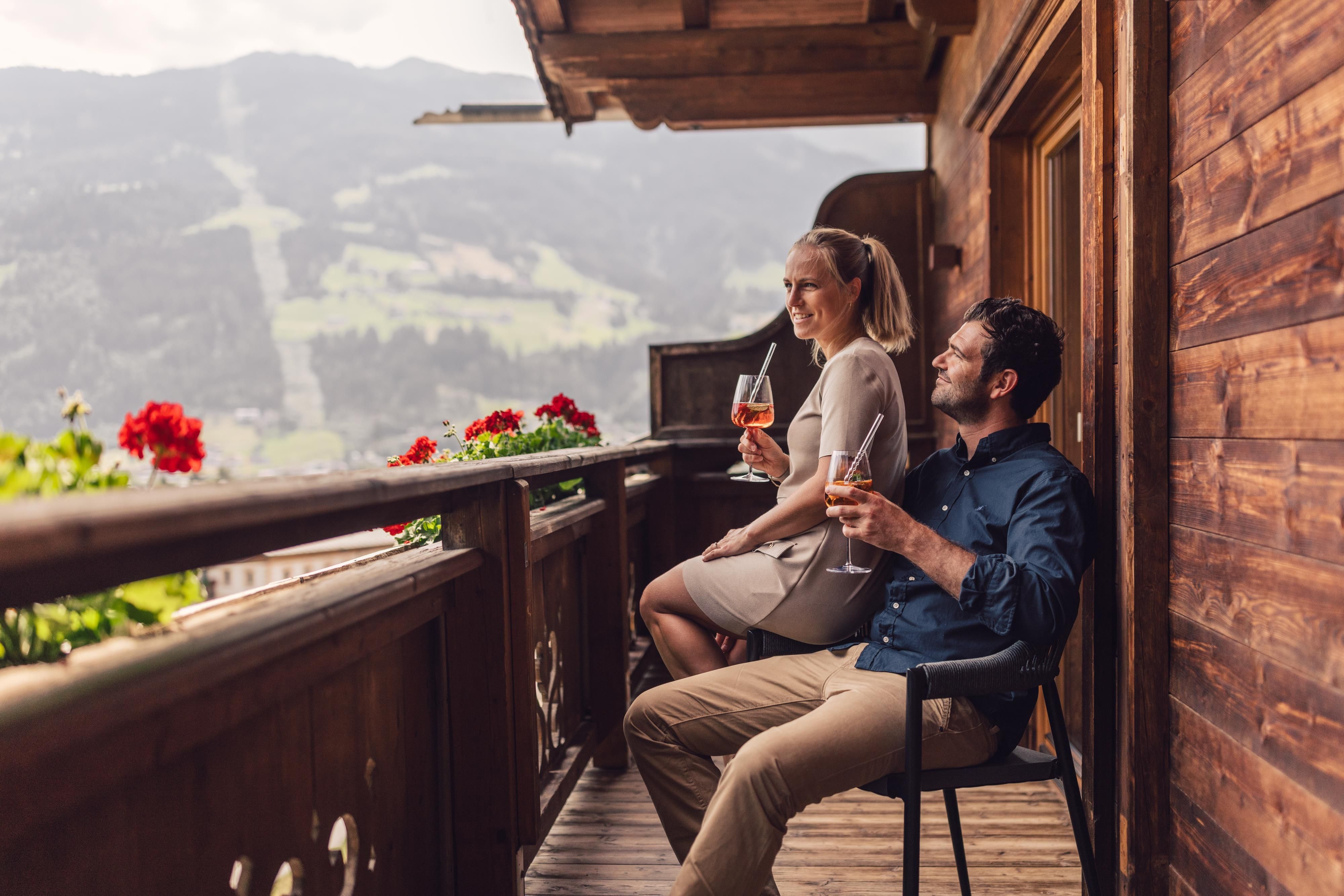 A couple is sitting relaxed on a balcony and enjoying drinks. In the background, the mountains and the landscape can be seen.