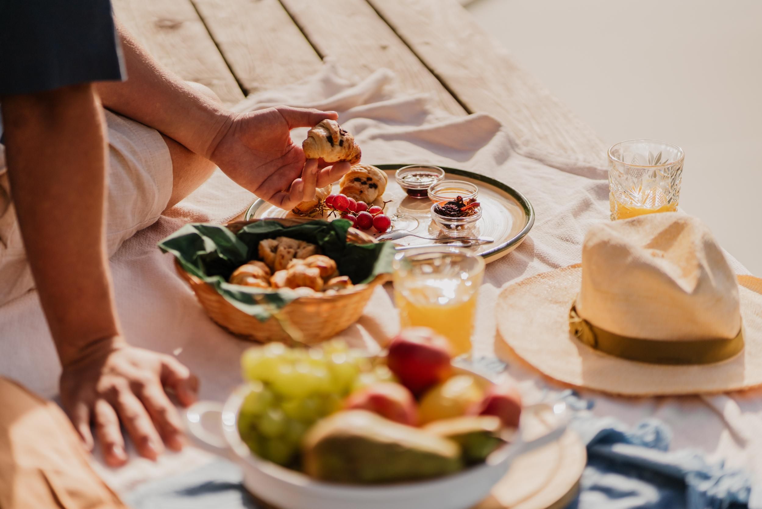 A cozy picnic on a wooden terrace with various treats. In the foreground, fruits, pastries, and a drink can be seen.