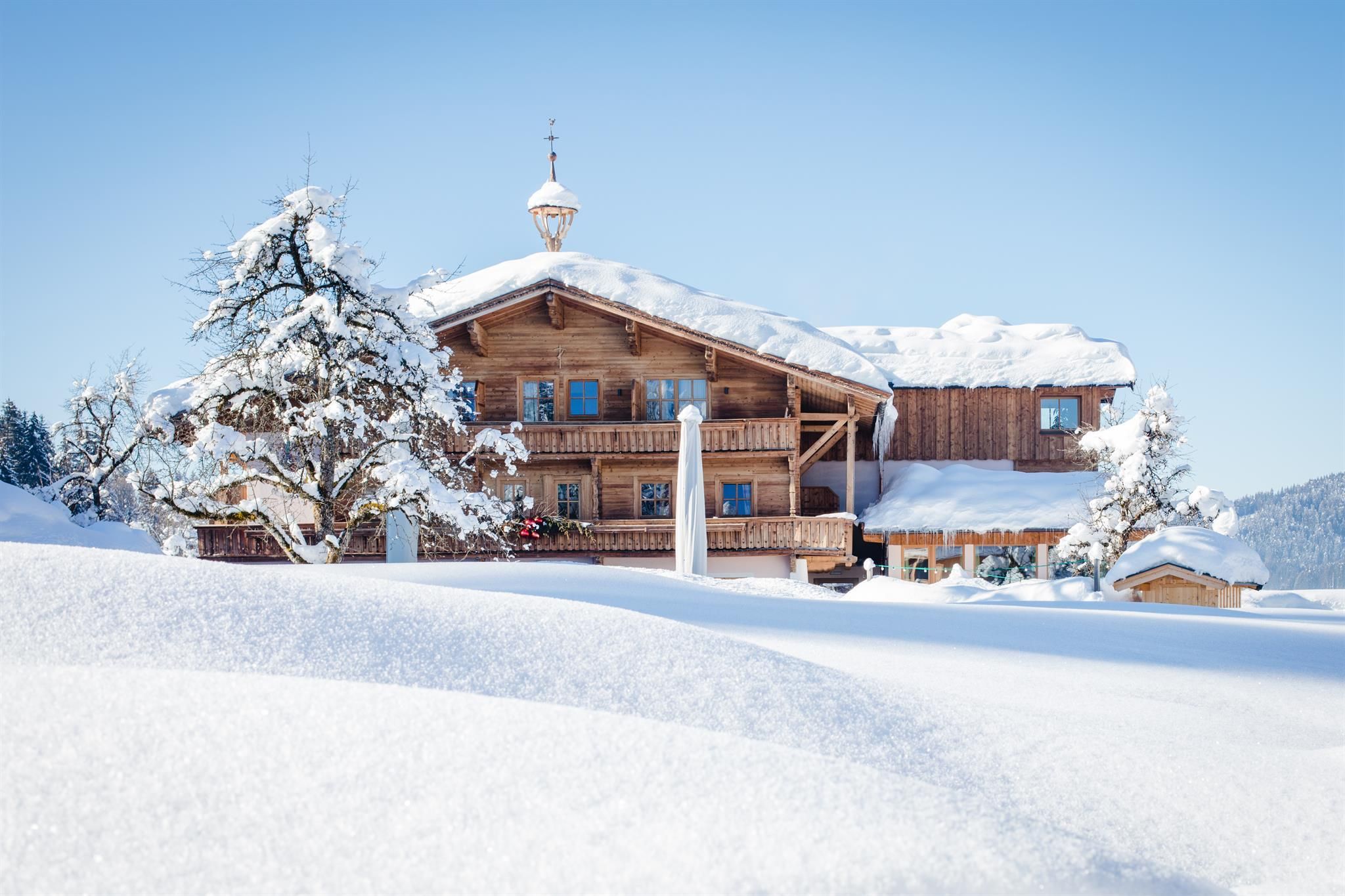 A charming wooden house in the snow, surrounded by wintry landscape. The clear sky and snow-covered trees give the scene a tranquil atmosphere.