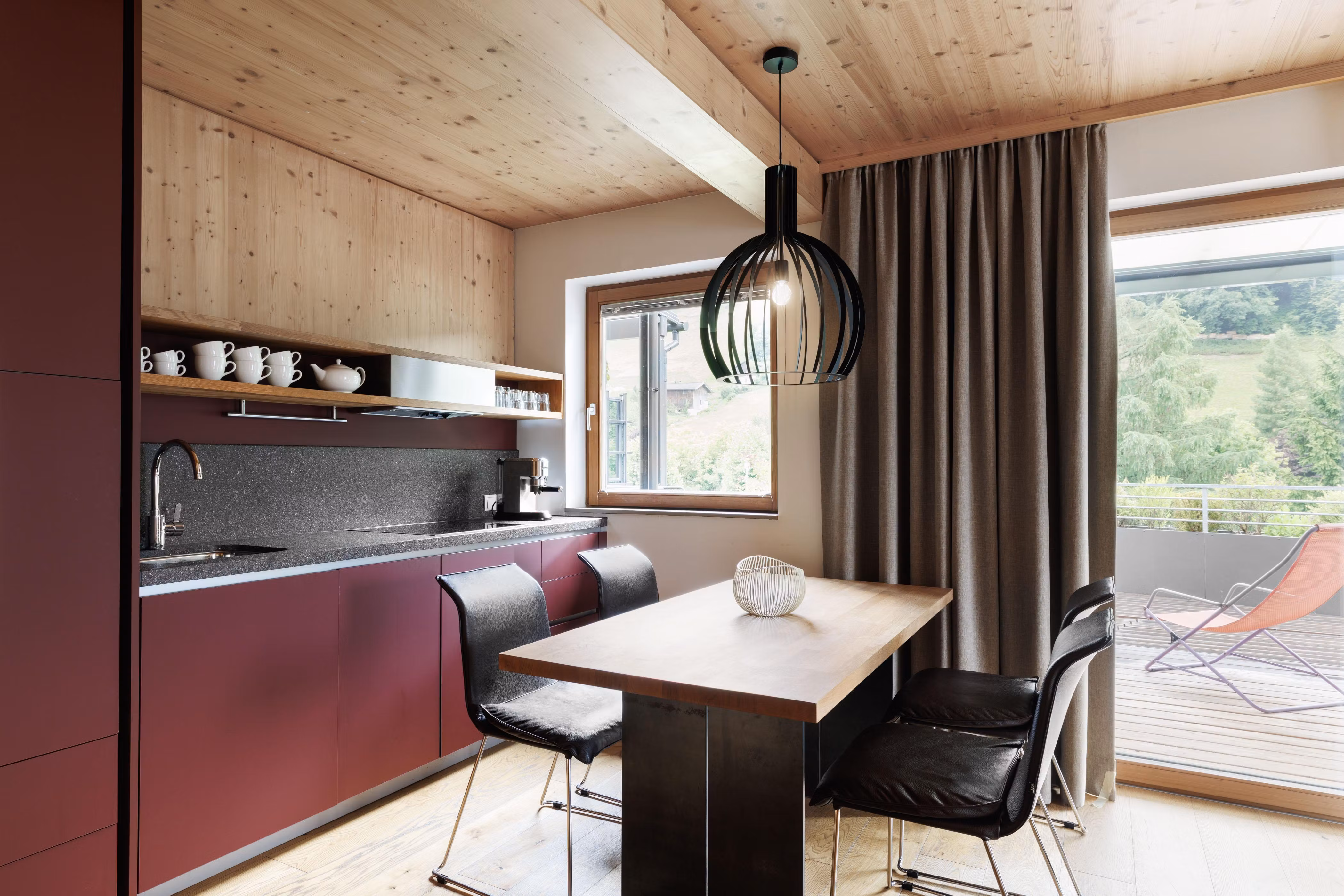 A modern kitchen with wood details and a large window. The table is made of wood and the chairs are black.