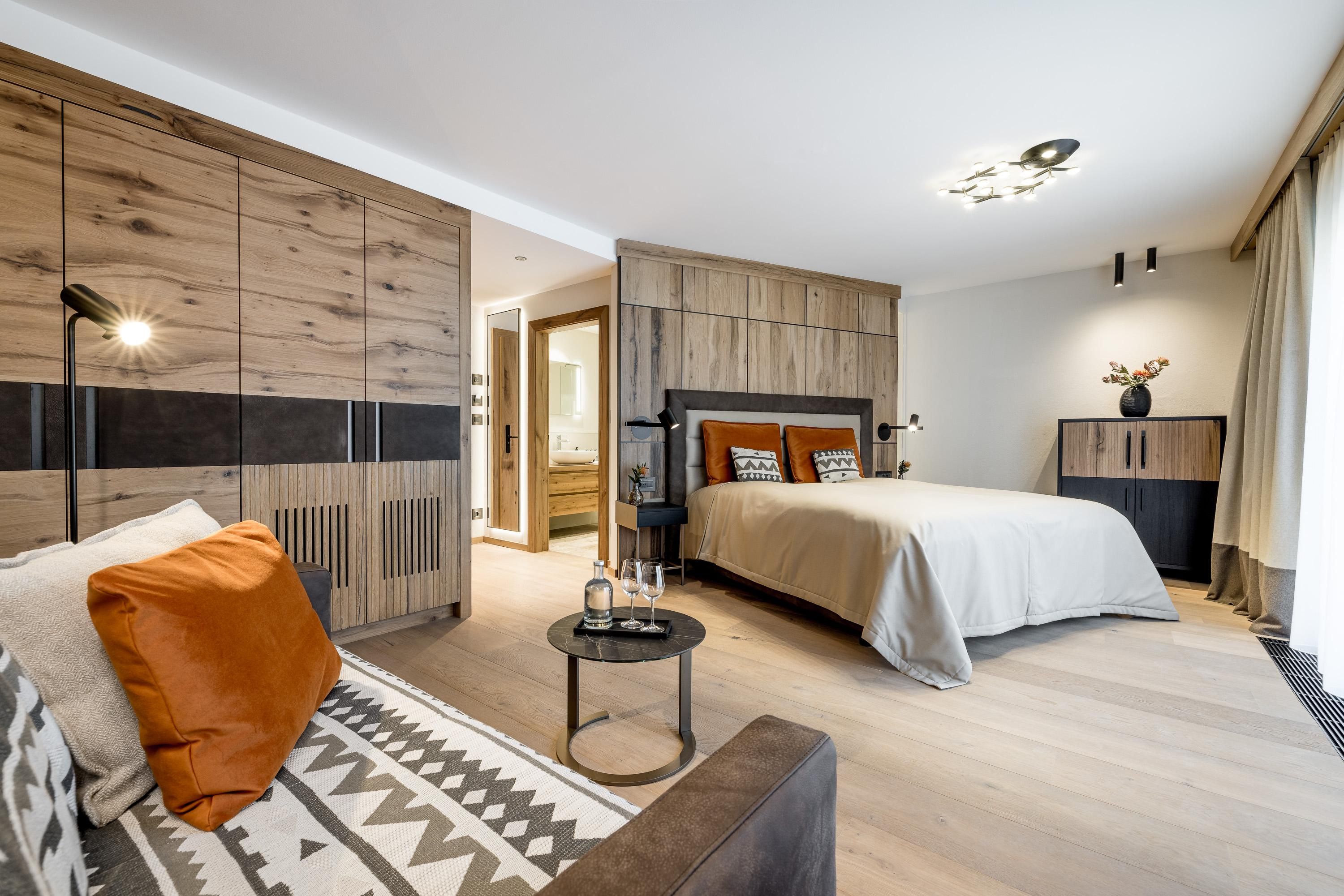 A modern bedroom with wood decor and a cozy atmosphere. There is a large bed, a small table, and a stylish seating area.
