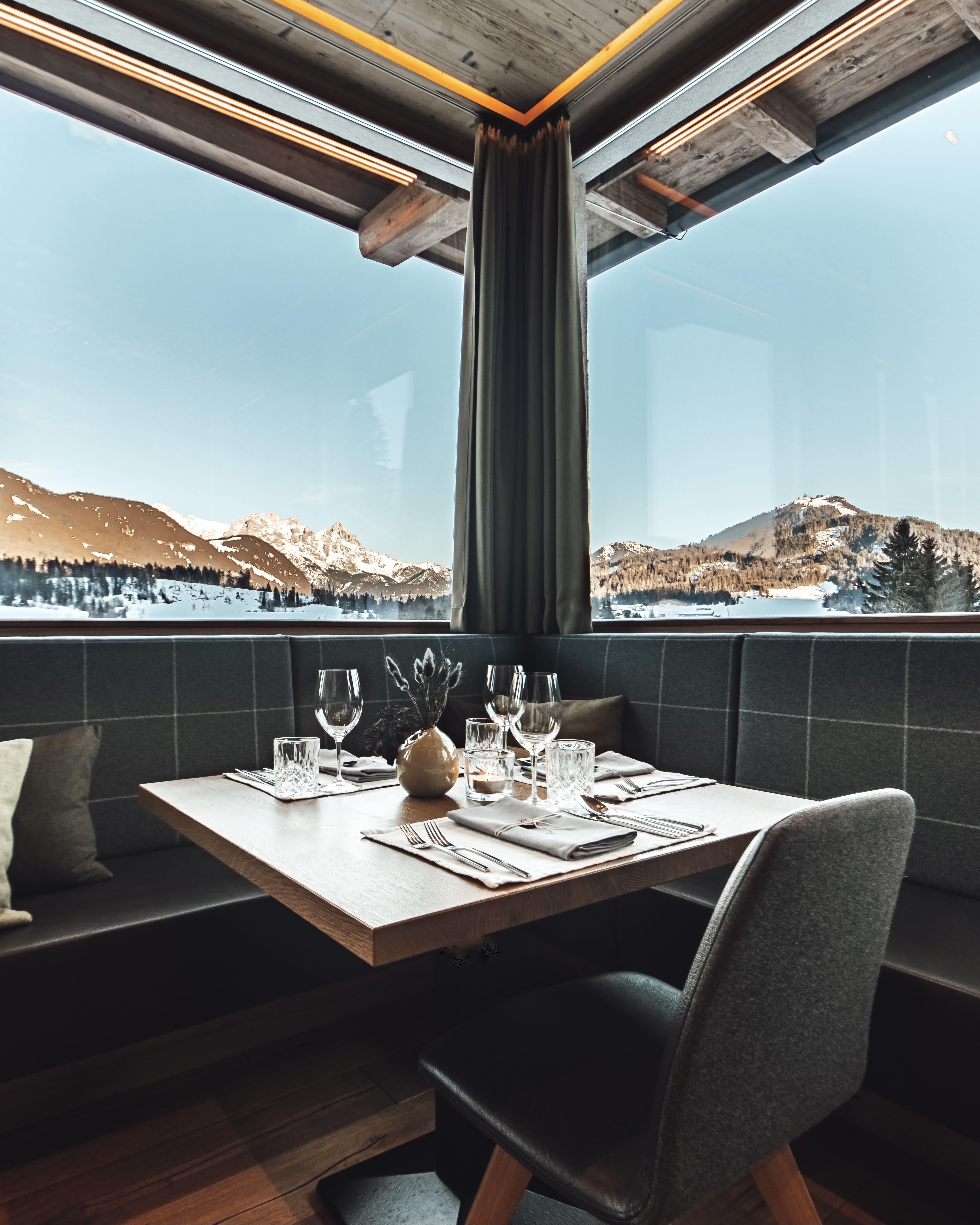 An elegant restaurant with a table for four people. Through large windows, there is a view of the snowy mountains and the blue sky.