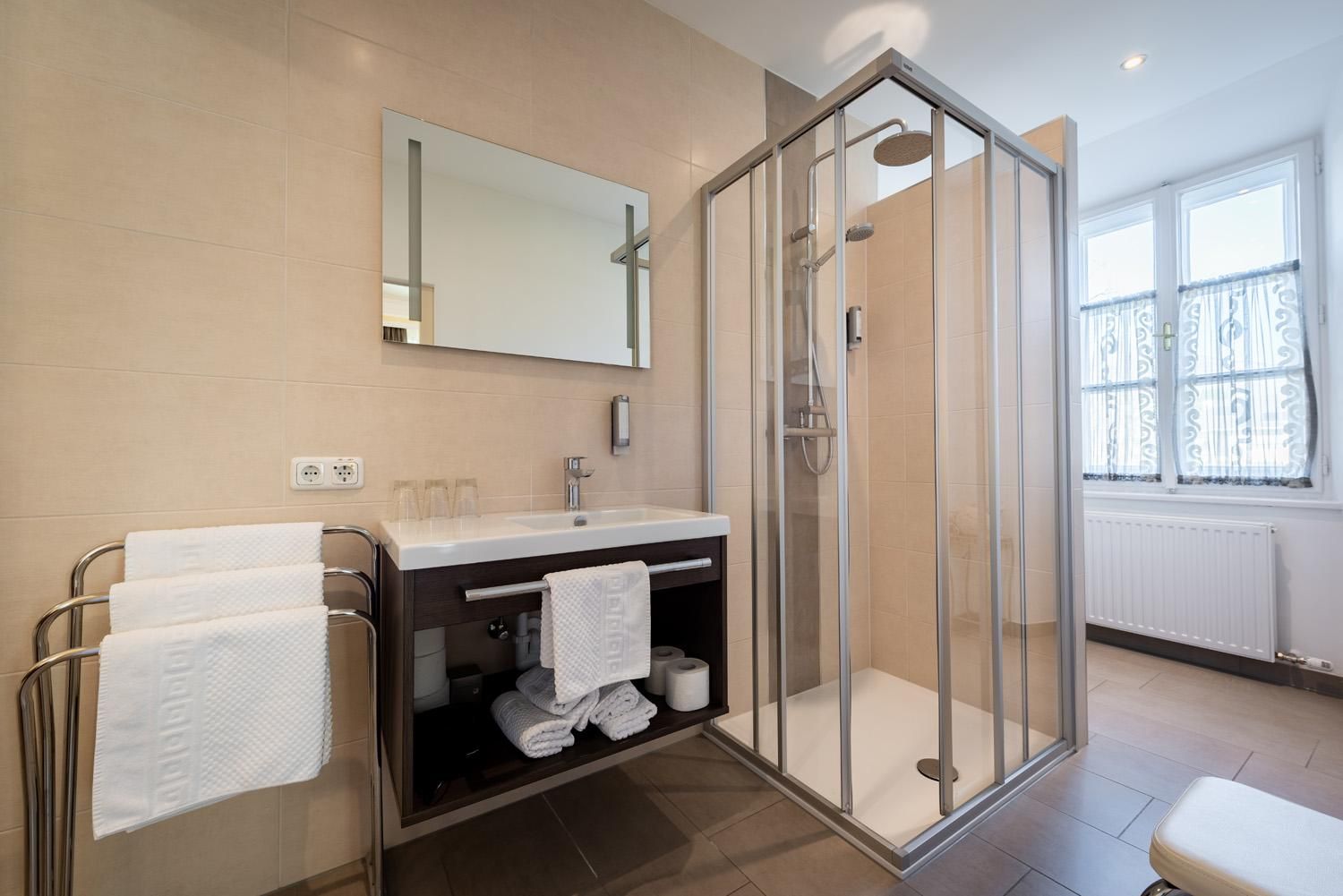 A modern bathroom with a transparent shower and a sink. Clean towels hang neatly on a rack.