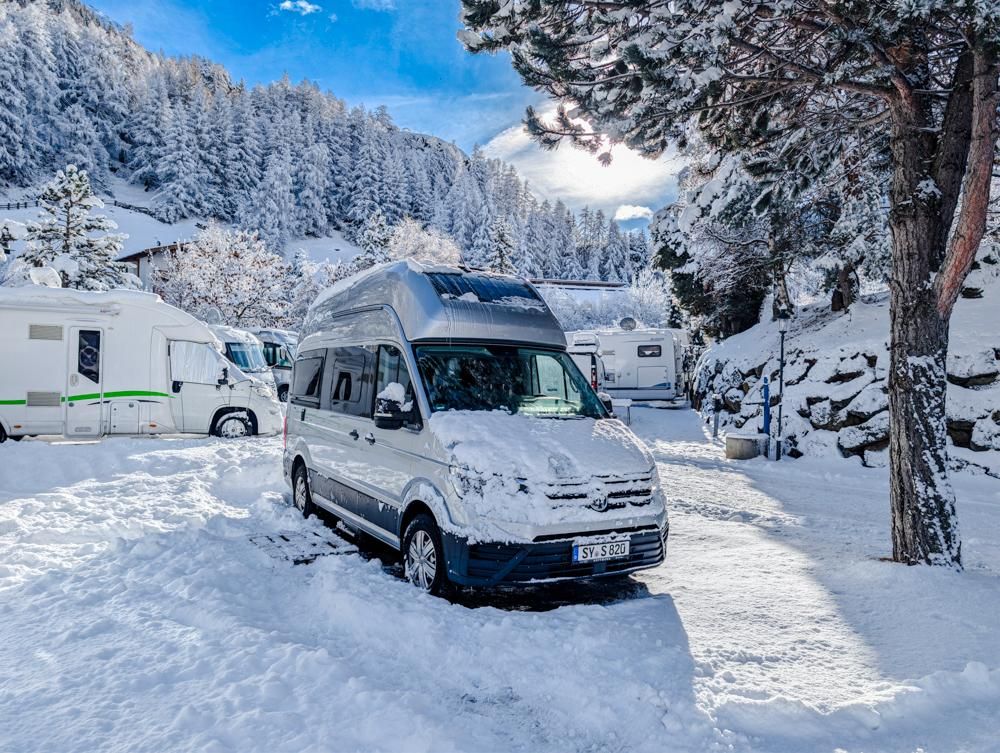 A motorhome is standing in a snow-covered environment. The trees and the sky are clear and display the winter landscape.